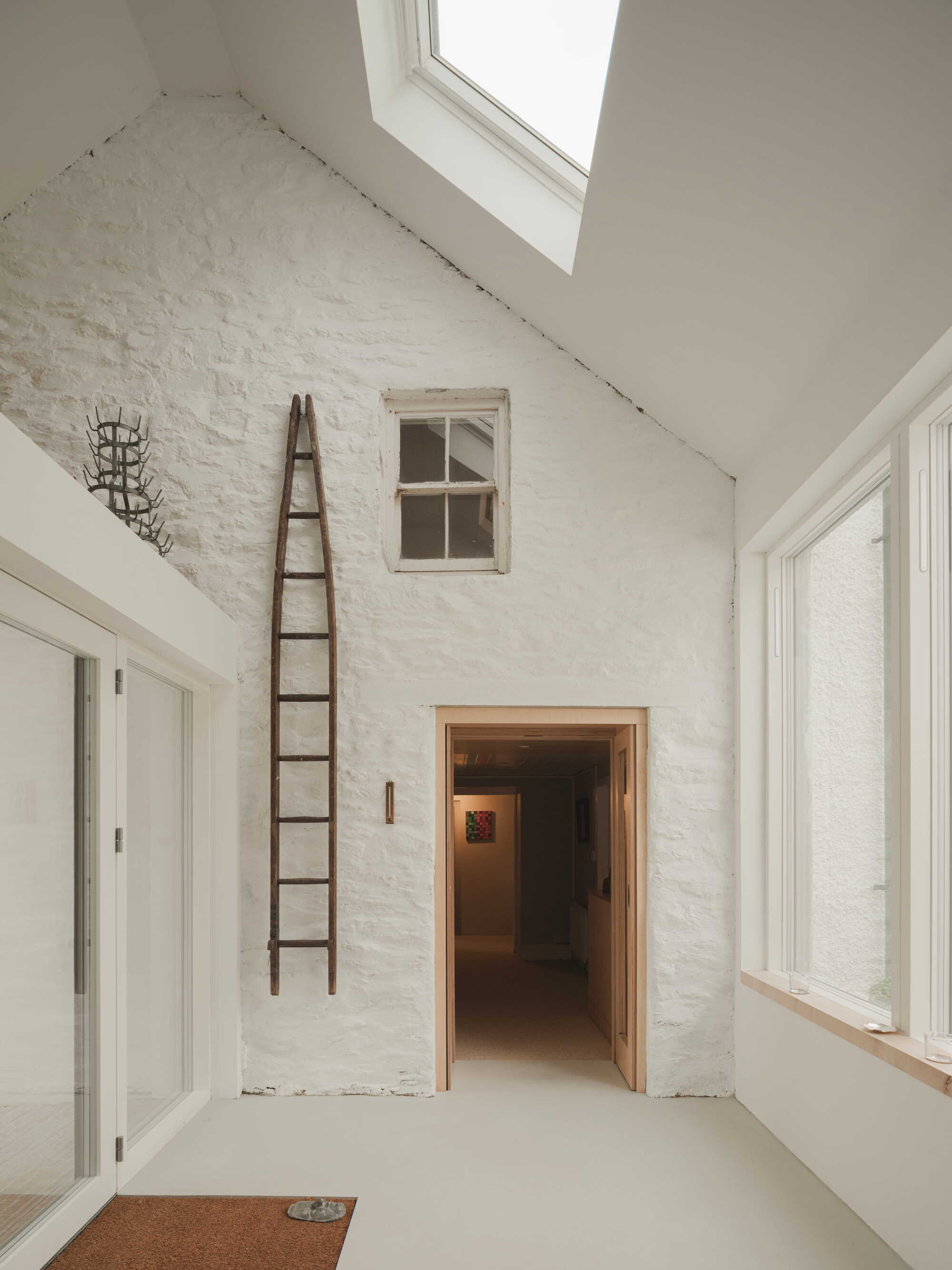 Double-height room with painted brick wall, wooden ladder, and skylight casting natural light