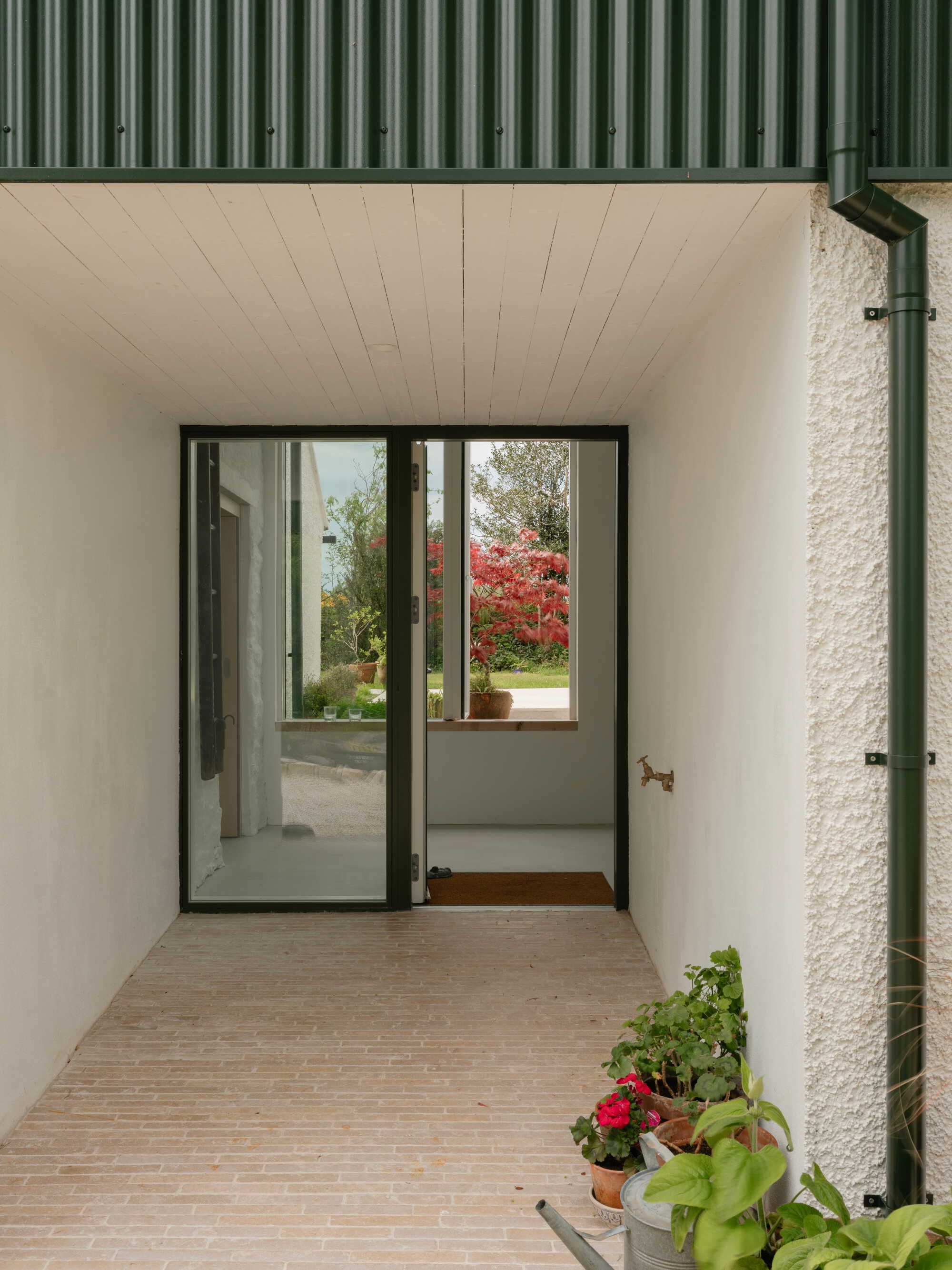 Covered exterior entry with timber decking and glazed door overlooking garden with red foliage