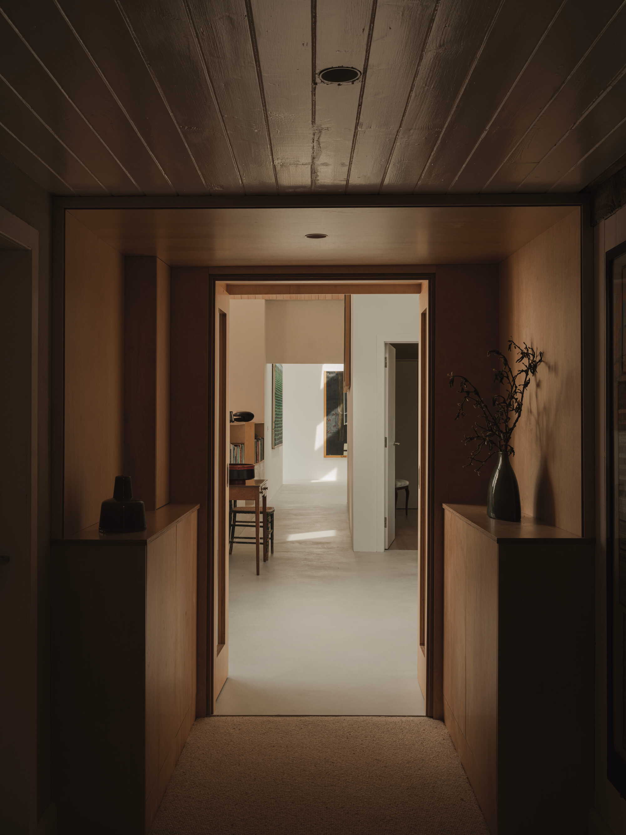 View through timber-framed doorway with wood plank ceiling leading to sunlit rooms beyond