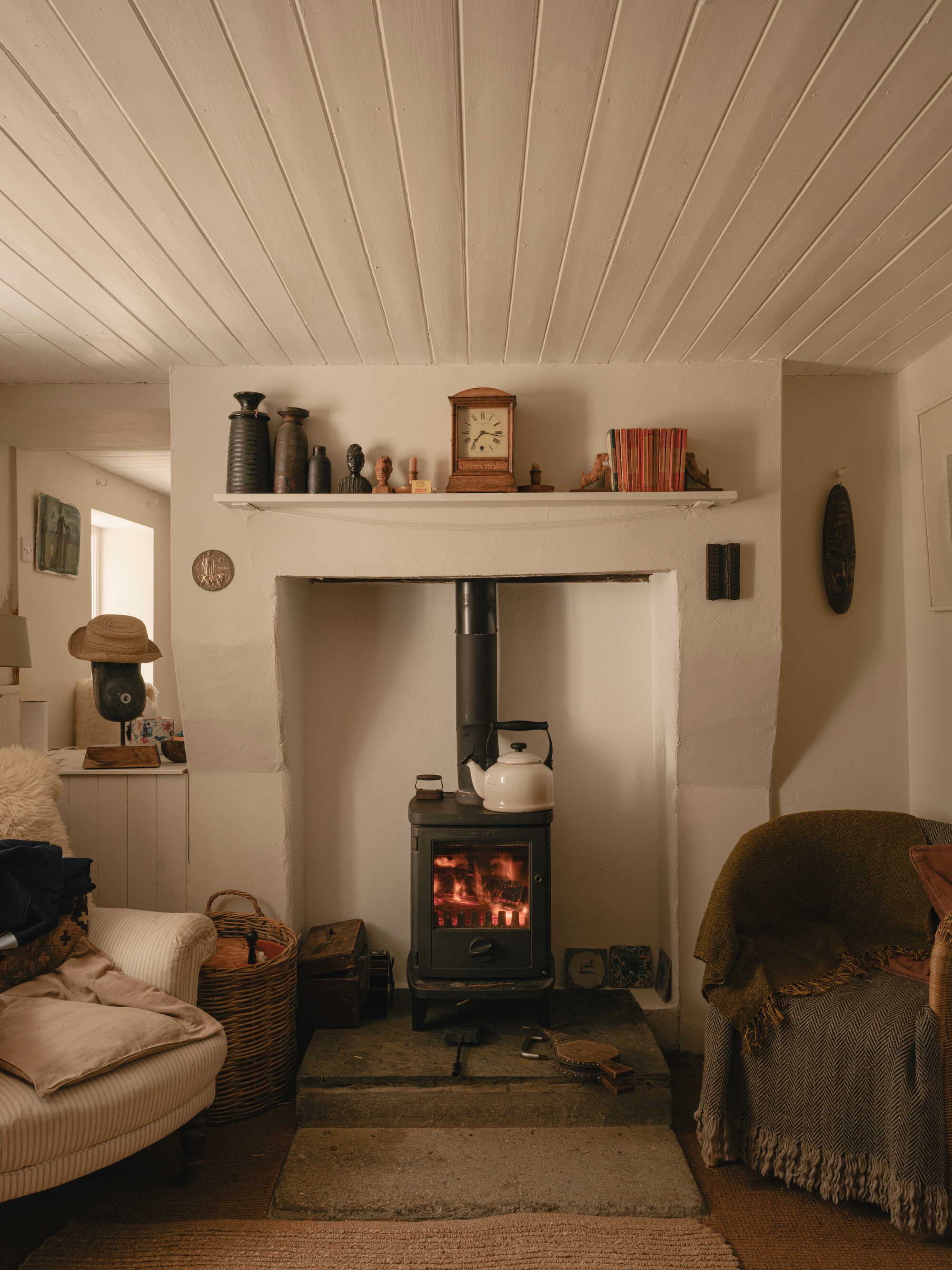 White plastered fireplace alcove with wood-burning stove and clay tile hearth in evening light