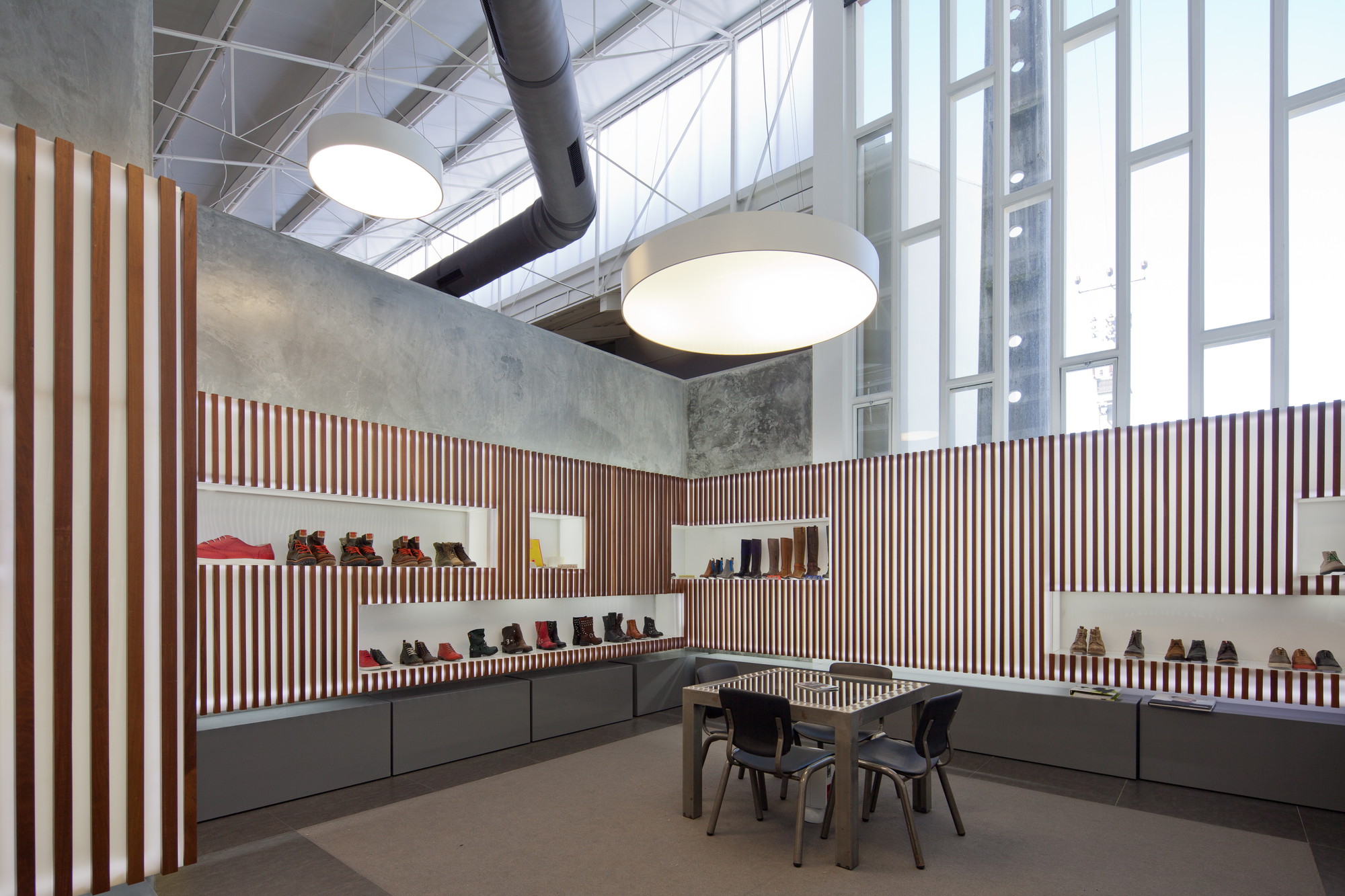 Showroom with striped timber walls, recessed shoe shelves, round pendant lamps and a tall glazed wall letting in daylight