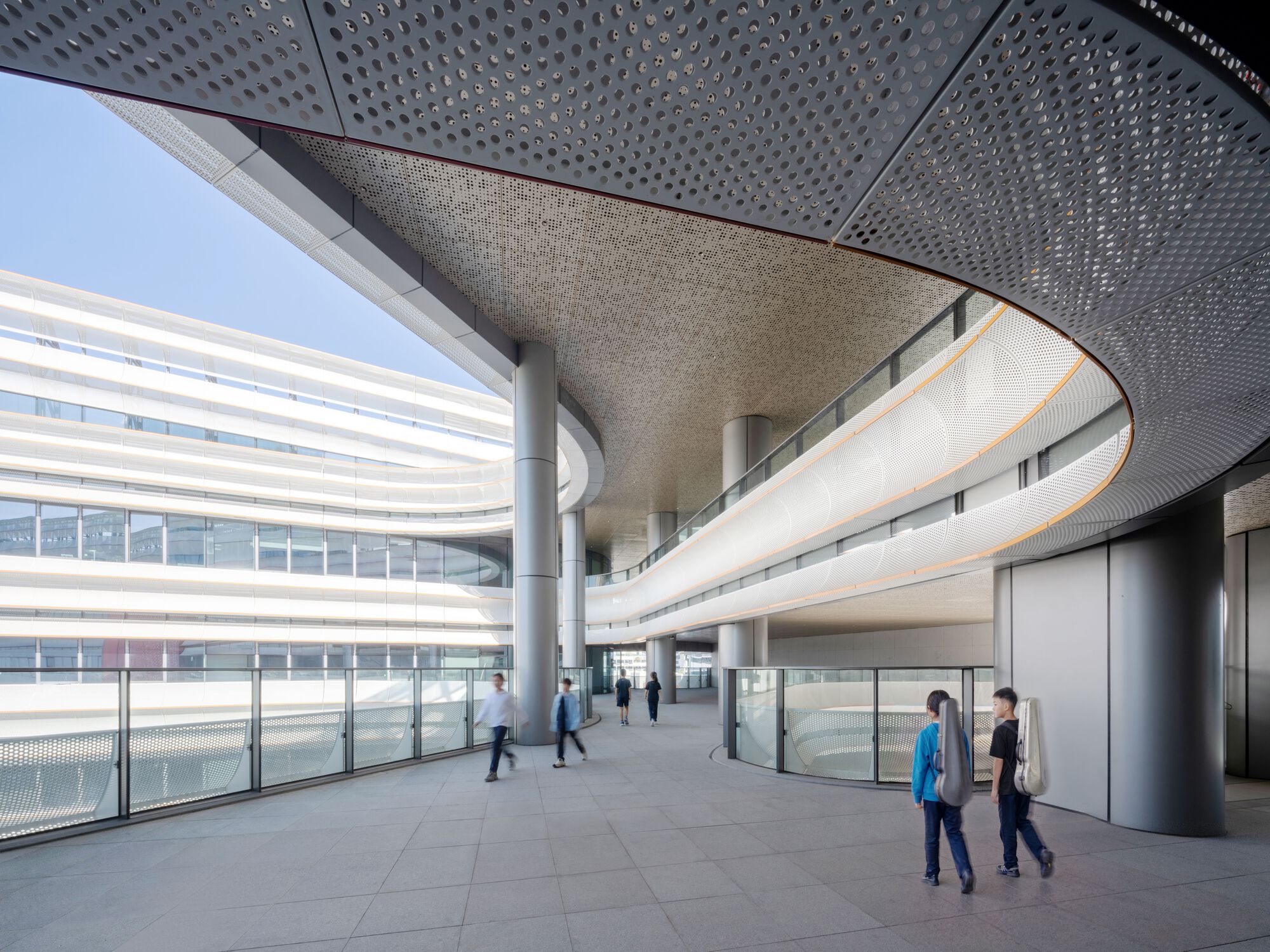Interior corridor with perforated ceiling panels and curved balconies overlooking the ground floor circulation space