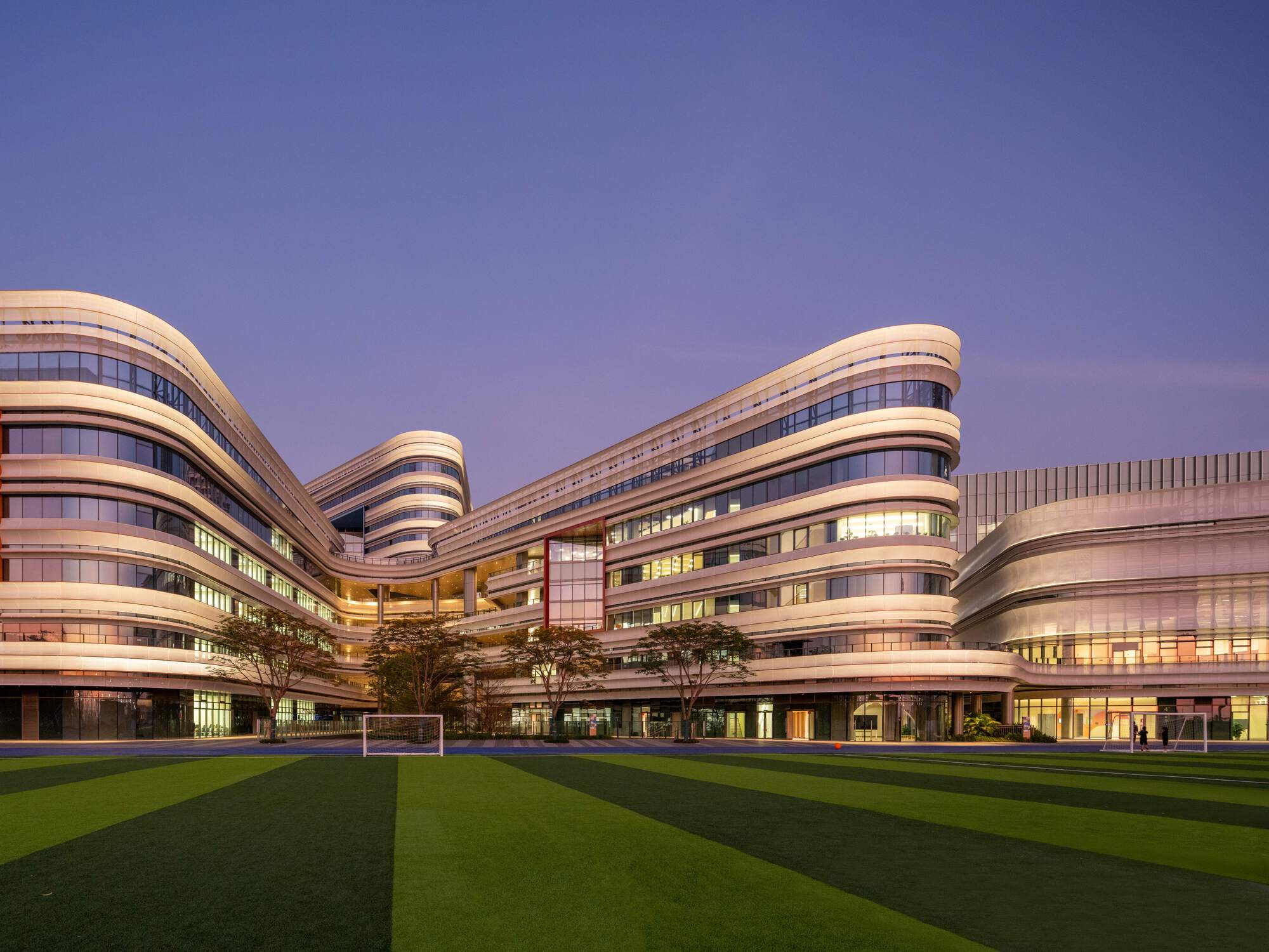 Campus courtyard view showing interconnected horizontal facade bands and playing field at twilight