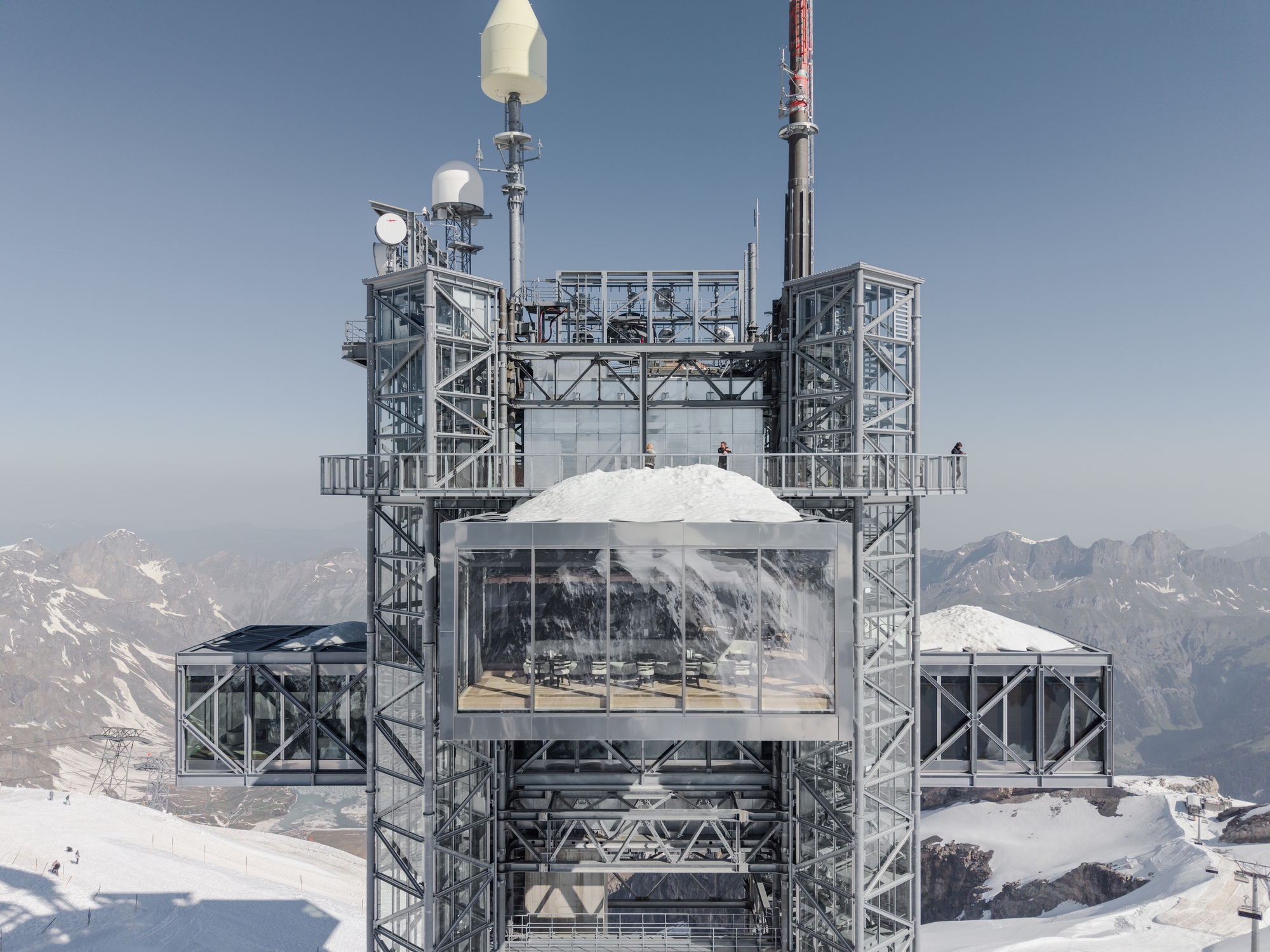 Frontal view of the steel framework with enclosed glass volume and snow-capped dome above mountain range