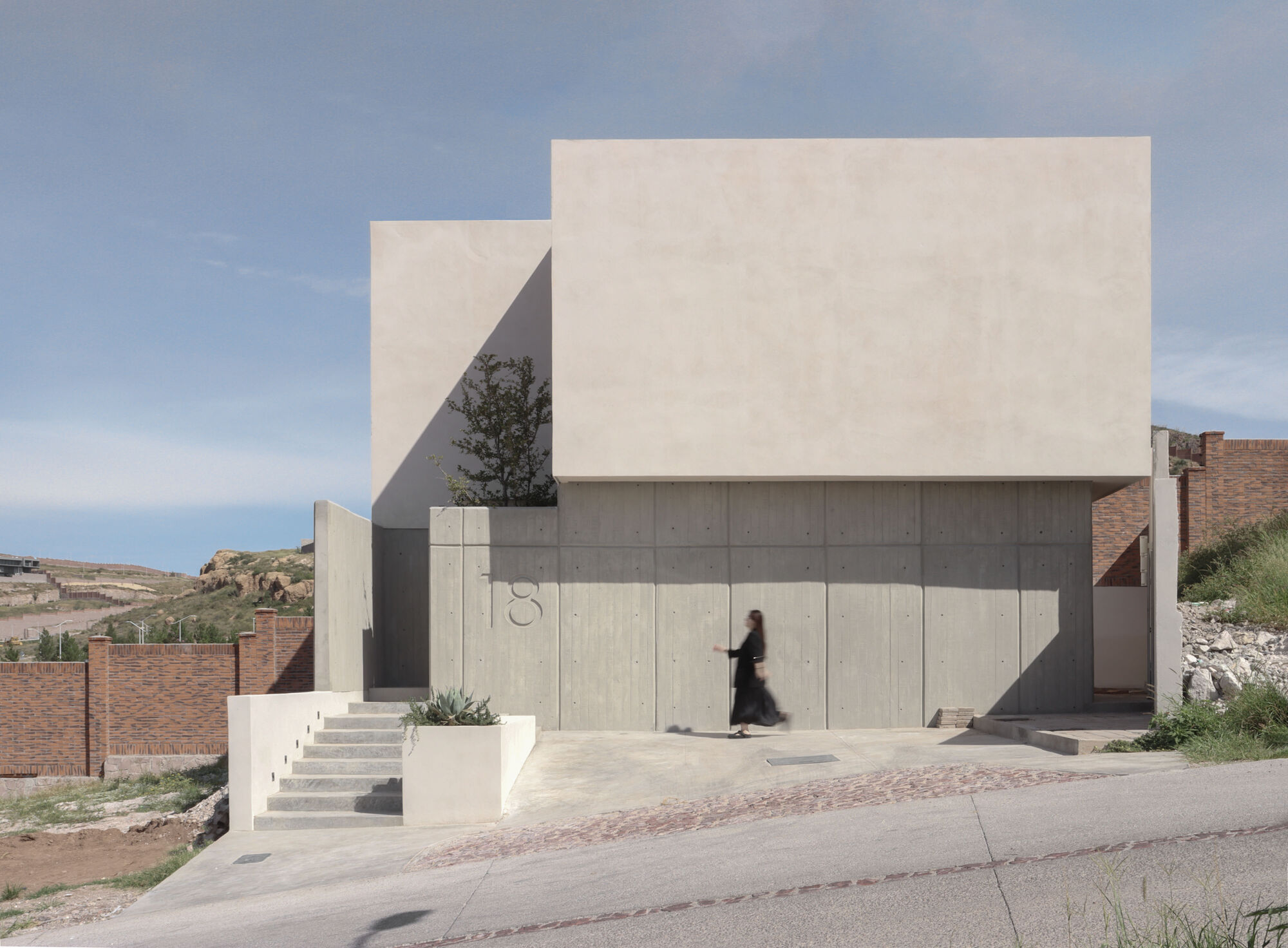Street view of the concrete and stucco facade with a figure passing the entrance wall