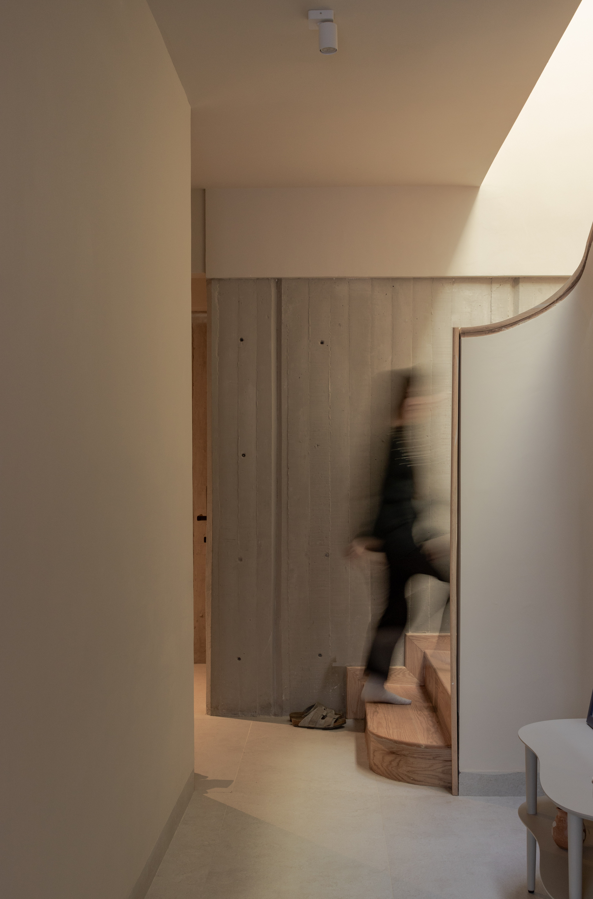 Interior hallway with curved timber stair rail and a blurred figure ascending in soft light