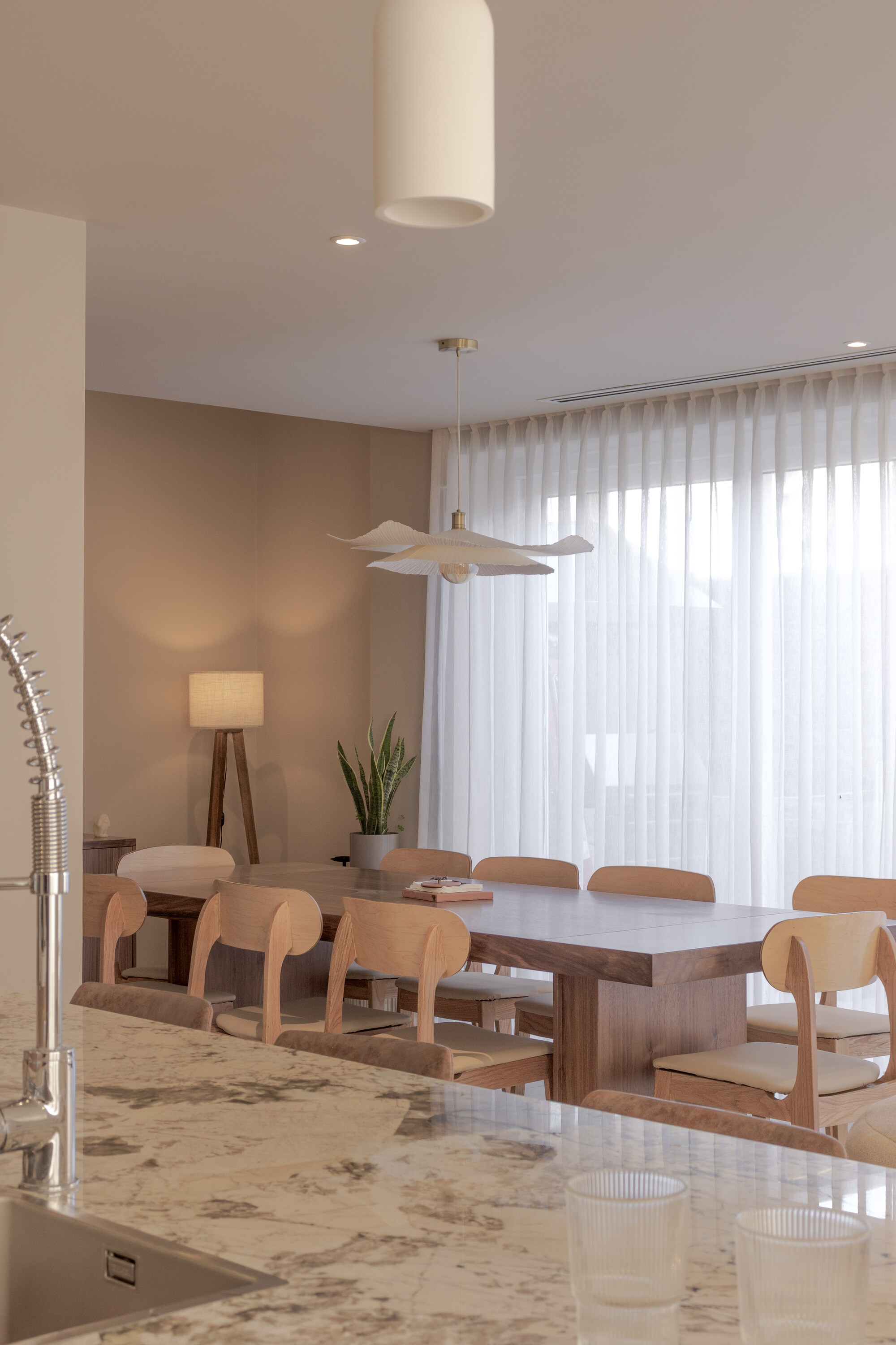 Dining area with timber table, curved-back chairs and sheer curtains filtering soft daylight