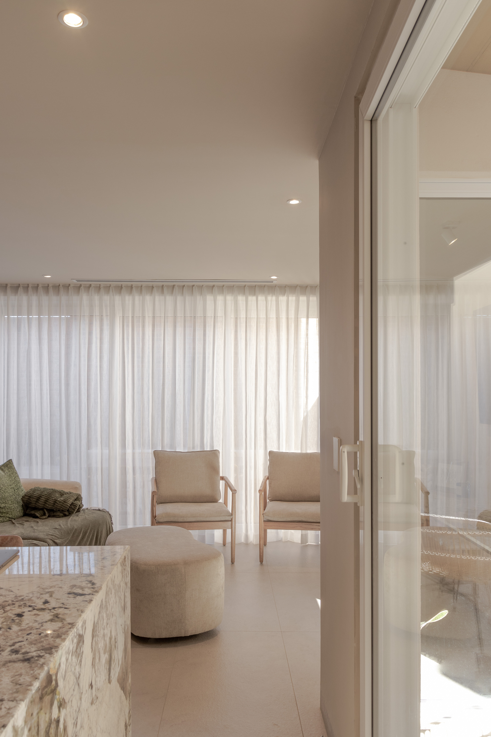 Living room with sliding glass door, upholstered chairs and floor-to-ceiling sheer drapes