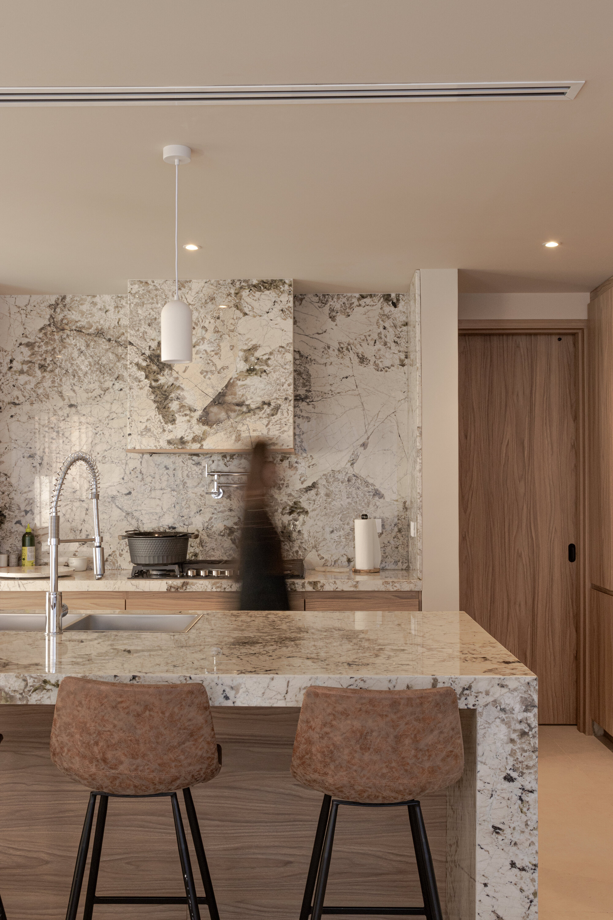 Kitchen island with veined stone countertop and backsplash as a figure passes through