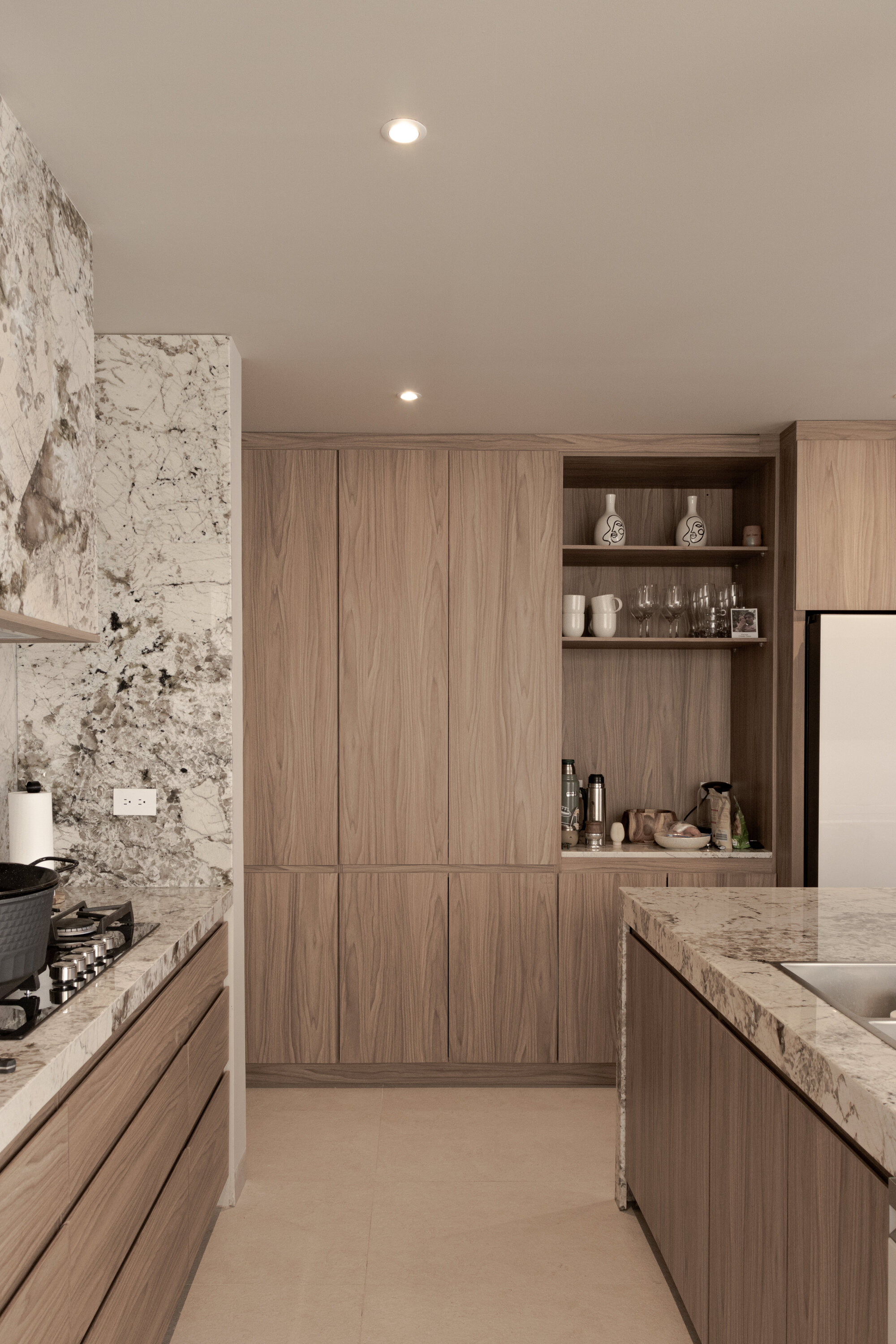 Kitchen cabinetry in pale timber veneer with open shelving and speckled stone counters