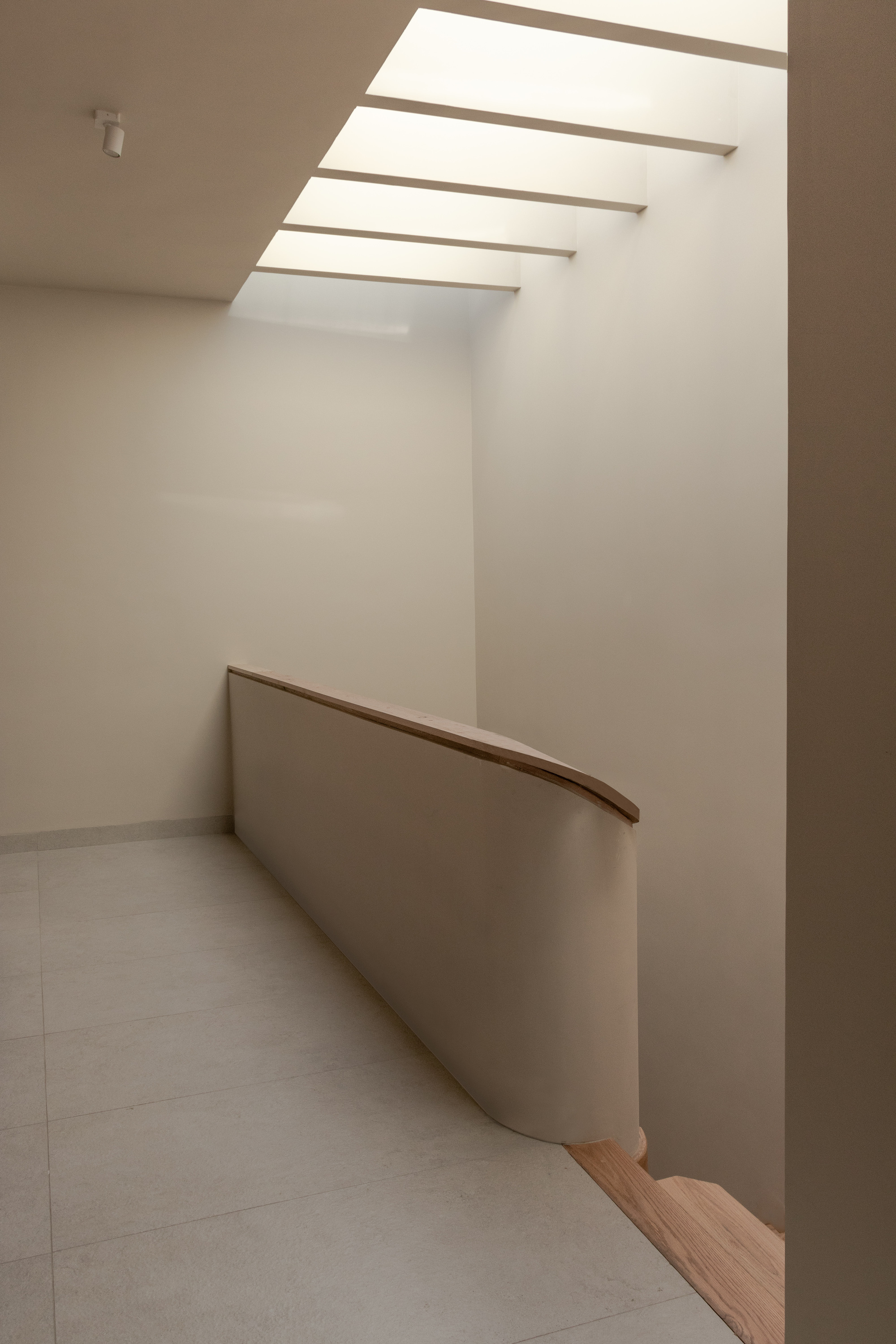 Curved timber handrail along a stair landing under a clerestory with horizontal beams