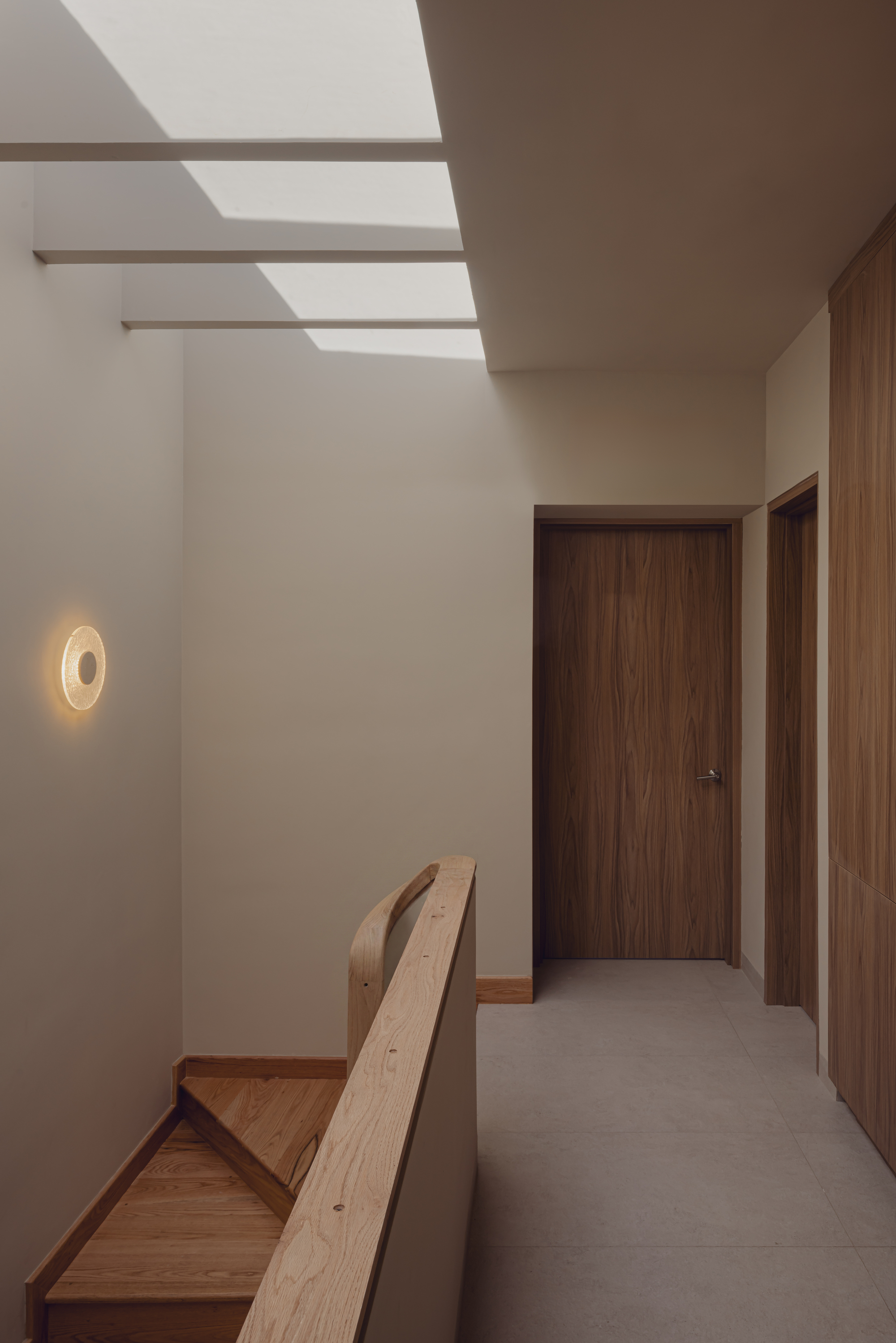 Upper hallway with timber doors and a wall sconce beneath a slatted skylight