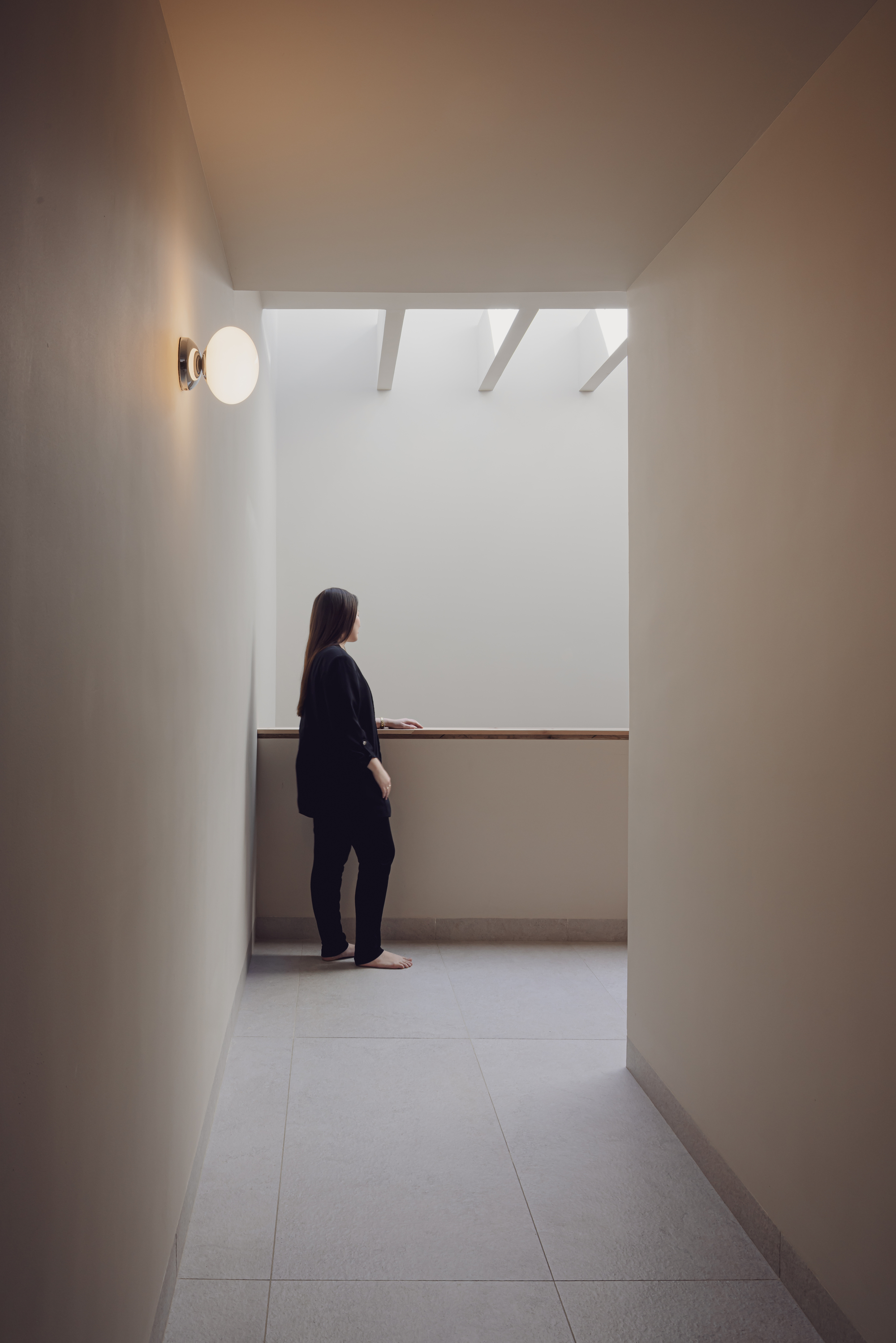 White hallway with exposed ceiling beams where a person stands beneath a wall sconce