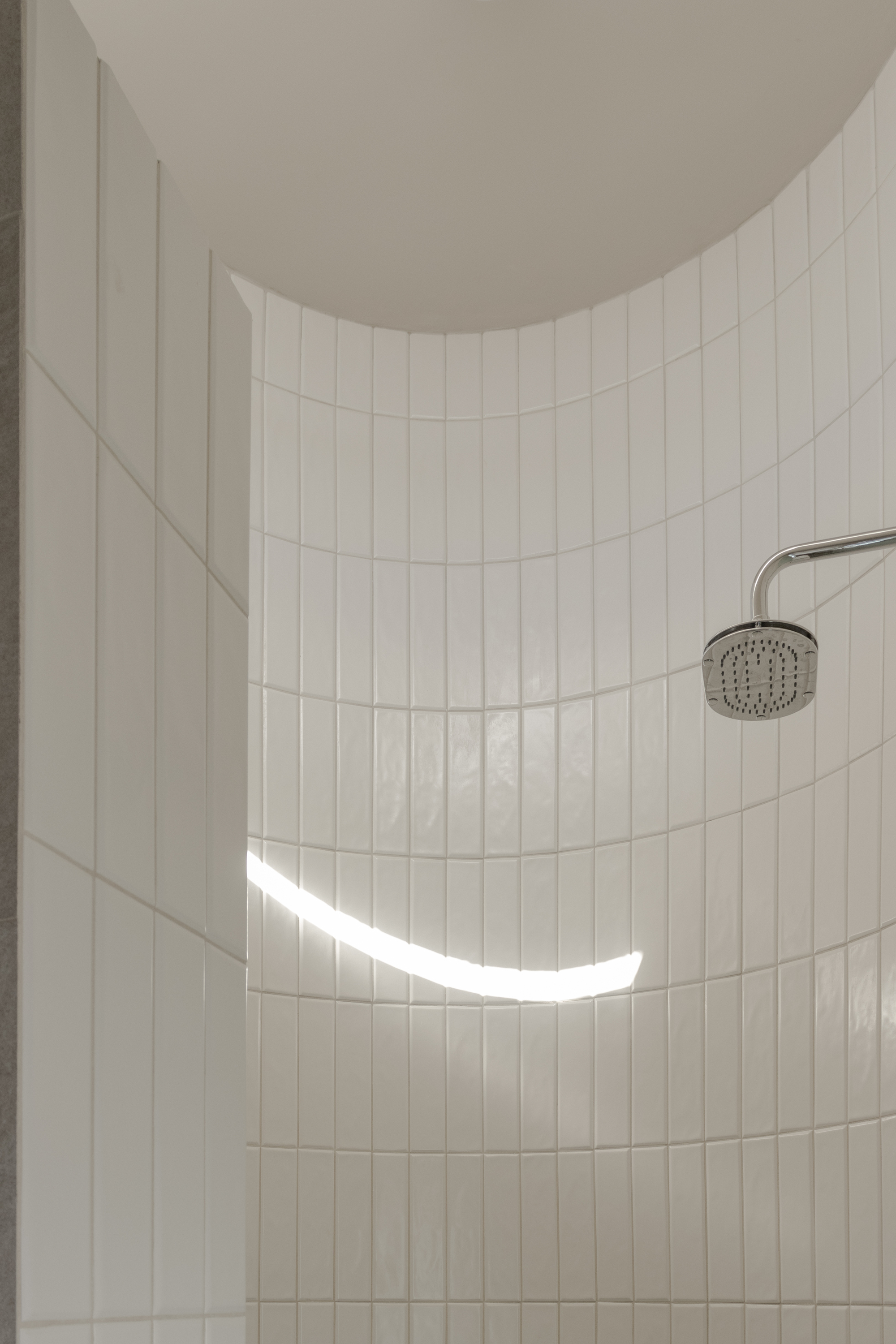 Curved white tile wall in shower with a thin horizontal window casting daylight