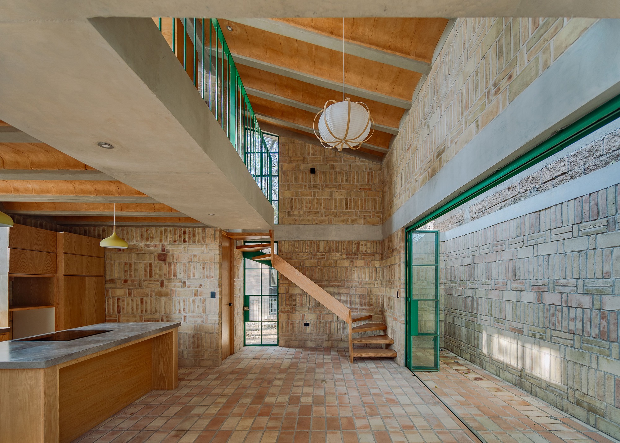 Double-height interior with exposed timber ceiling beams, textured brick walls, and a wooden stair ascending beneath a pendant light