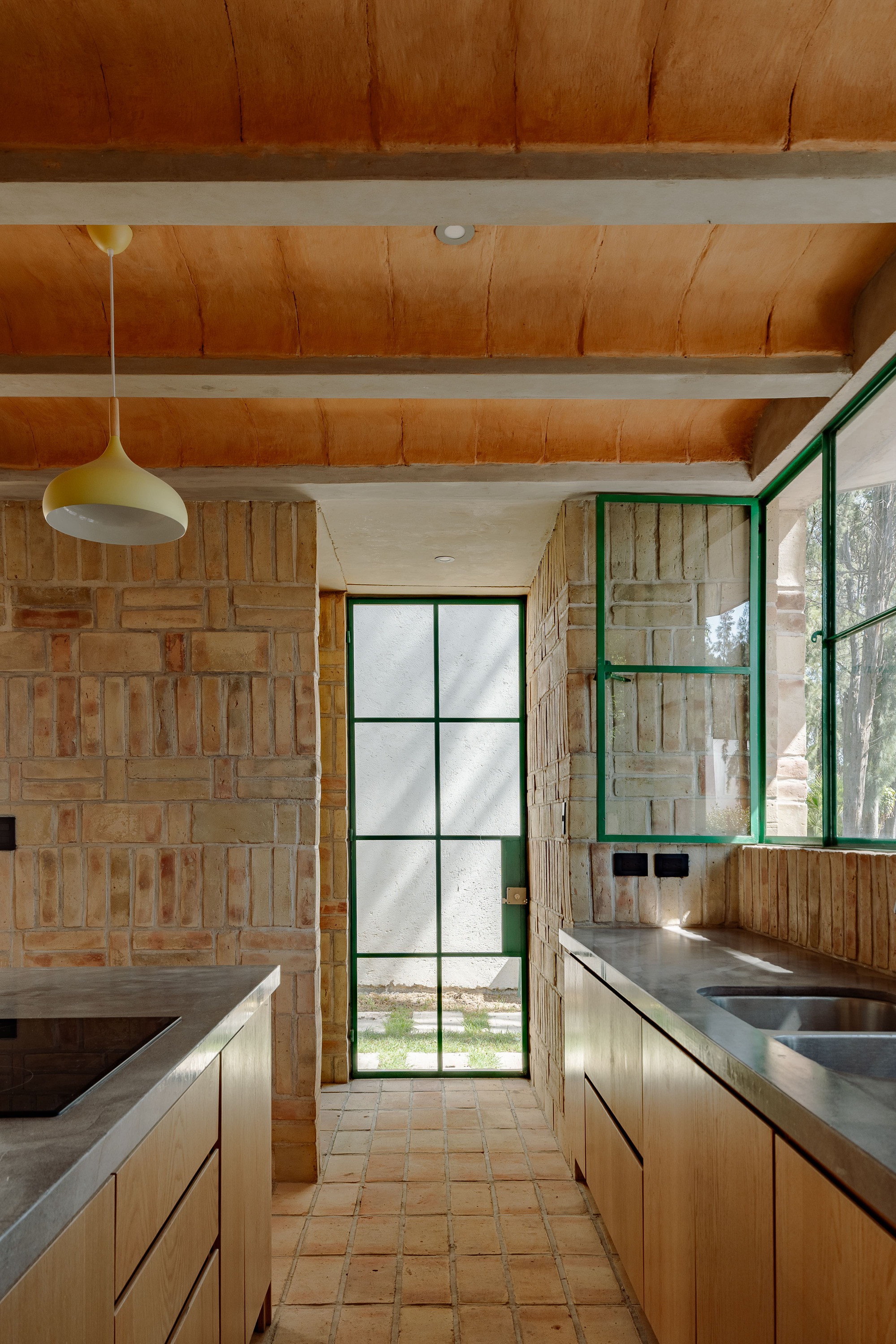 Galley kitchen with timber cabinetry, concrete countertops, and exposed ceiling beams lit by a pendant fixture