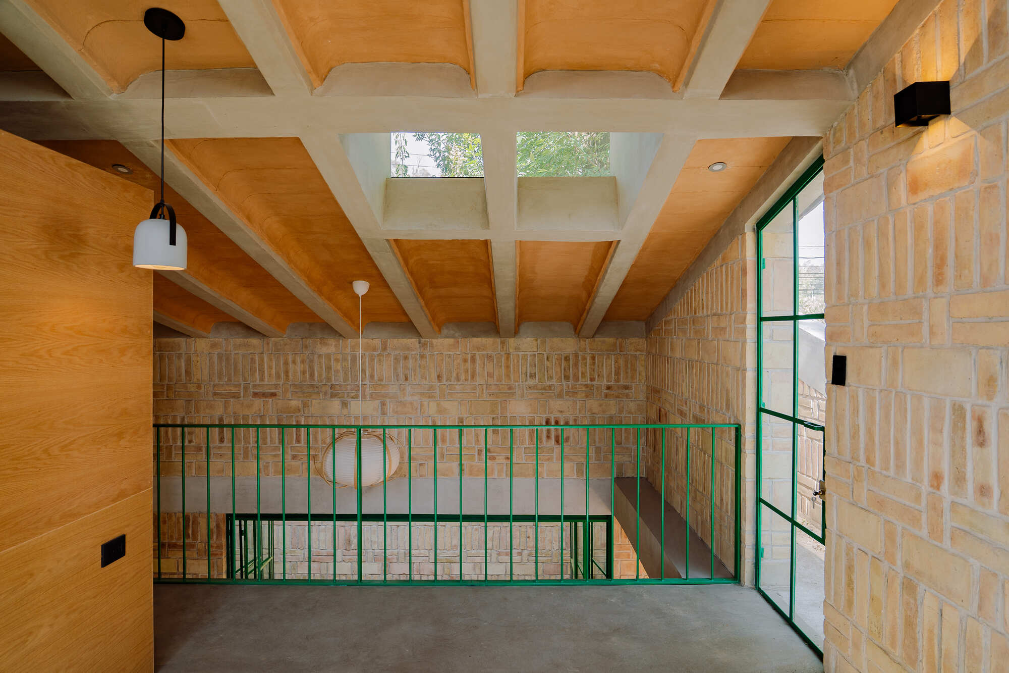 Upper level with green metal railing, exposed timber beams, and clerestory windows above textured brick walls