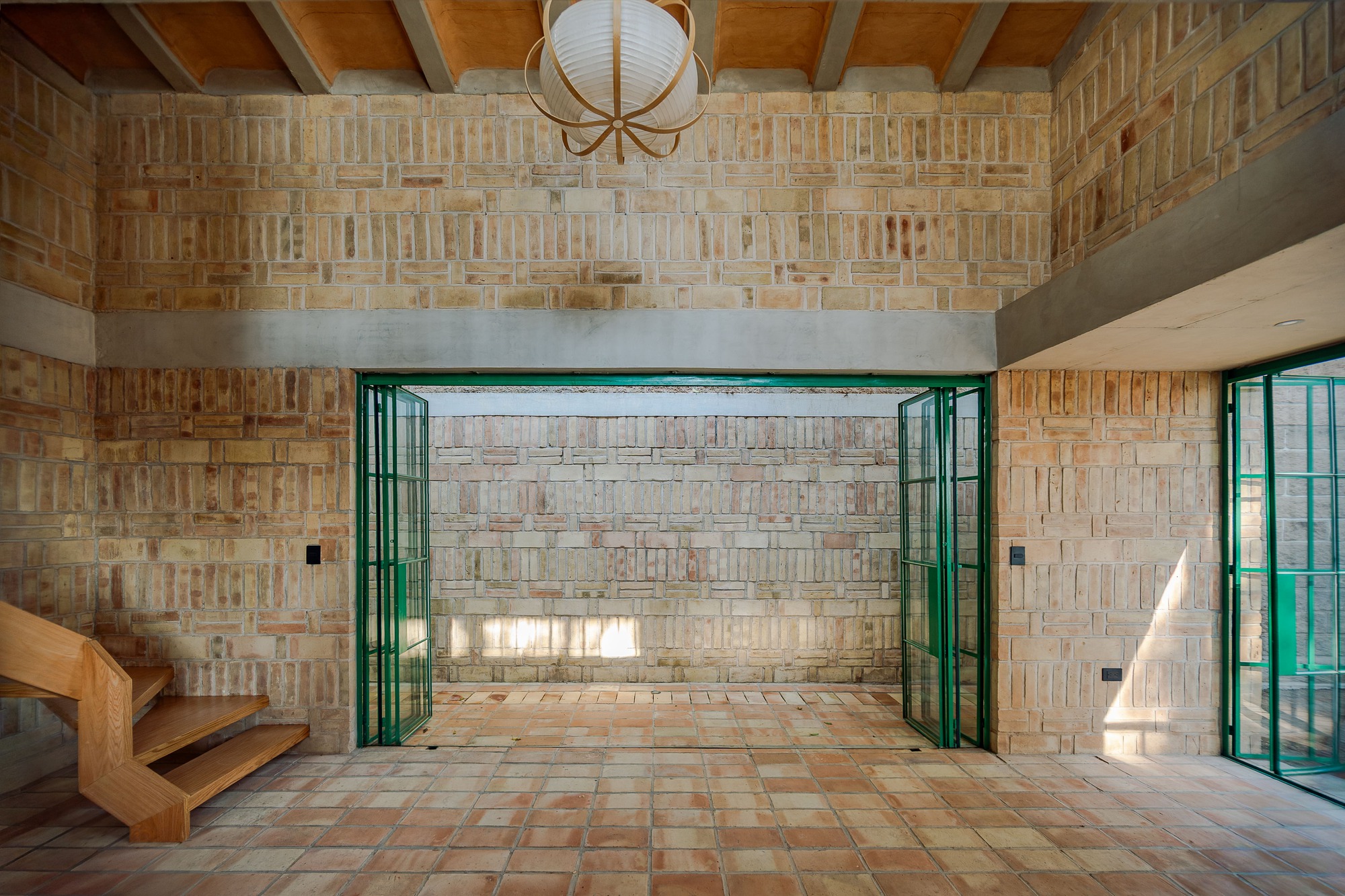 Interior view through open green-framed doors to textured brick courtyard wall with exposed timber ceiling beams