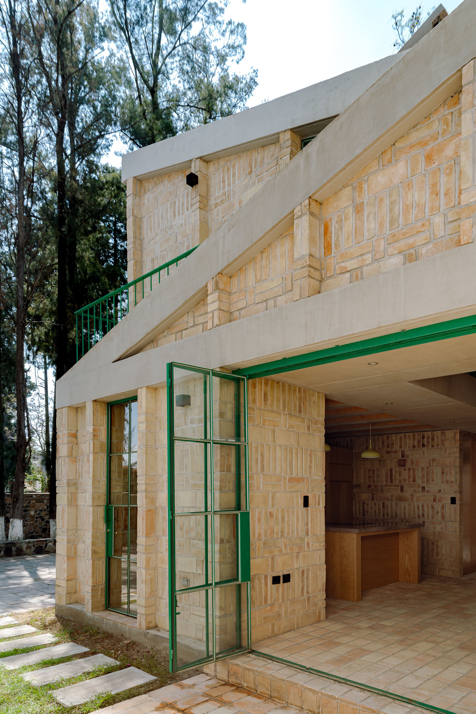 Angled facade showing recessed terrace with green-framed glazing and patterned brick walls under concrete overhang