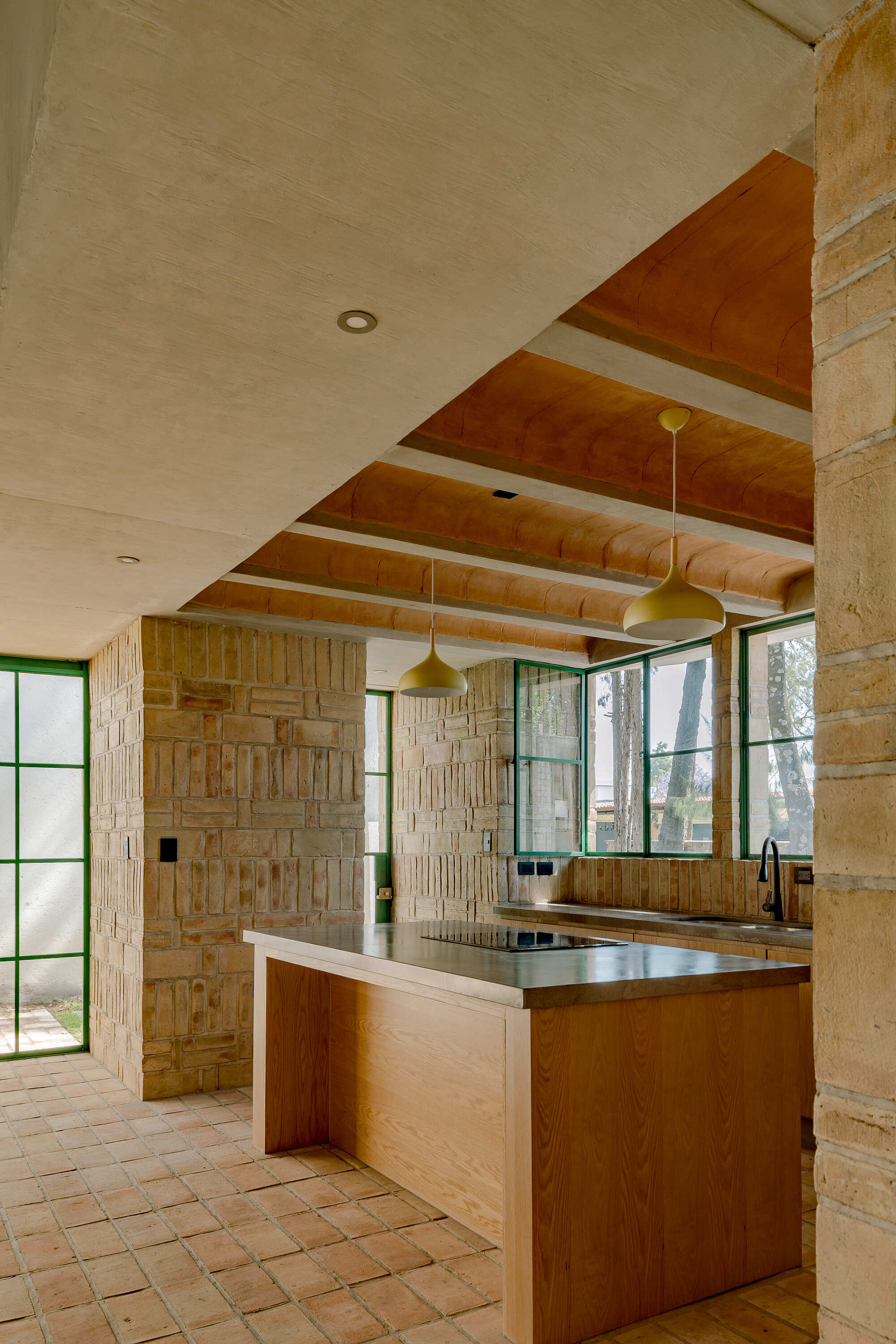 Kitchen island with stainless steel countertop beneath alternating flat and vaulted timber ceiling panels