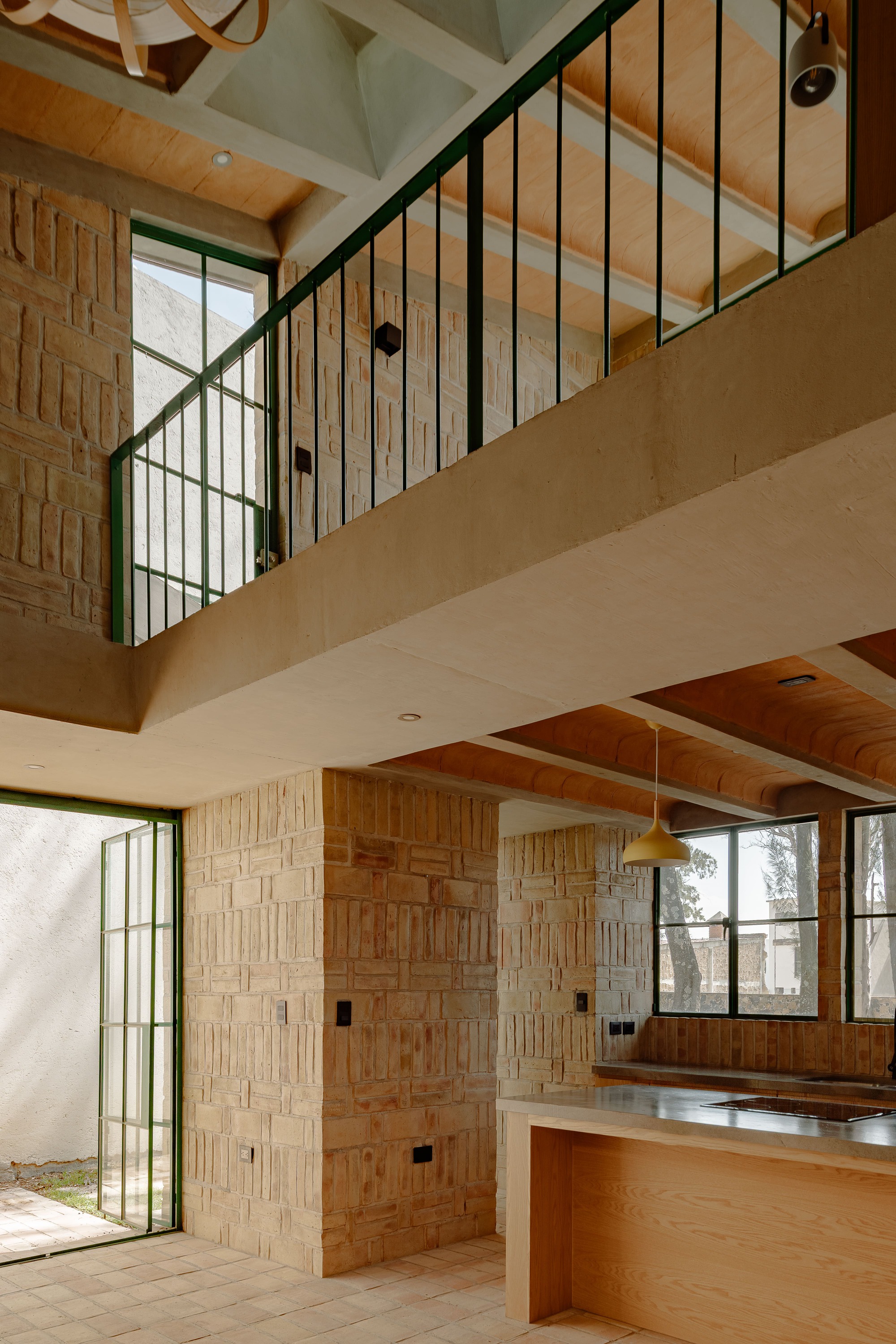Double-height space with kitchen island below mezzanine level and green metal railing against timber wall