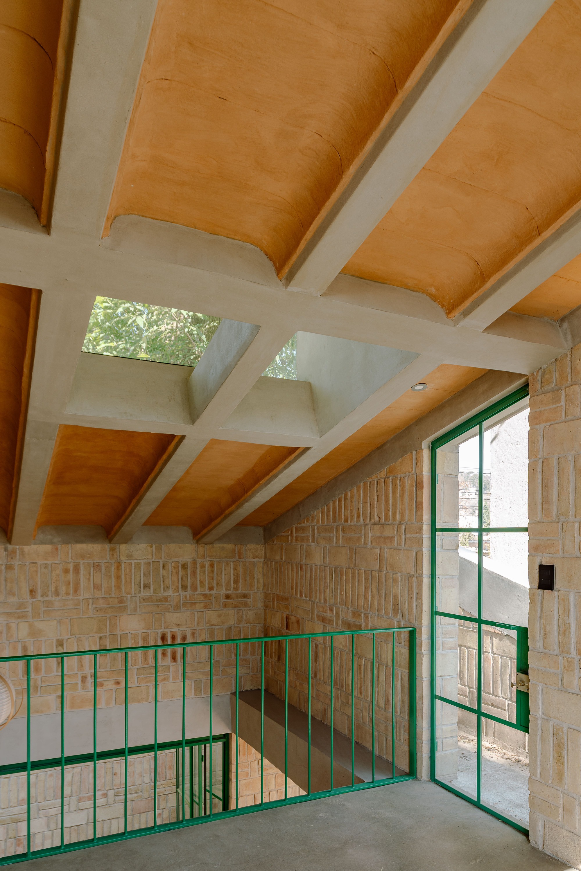 Upper landing with vaulted timber ceiling, white concrete beams, green steel railing and skylight