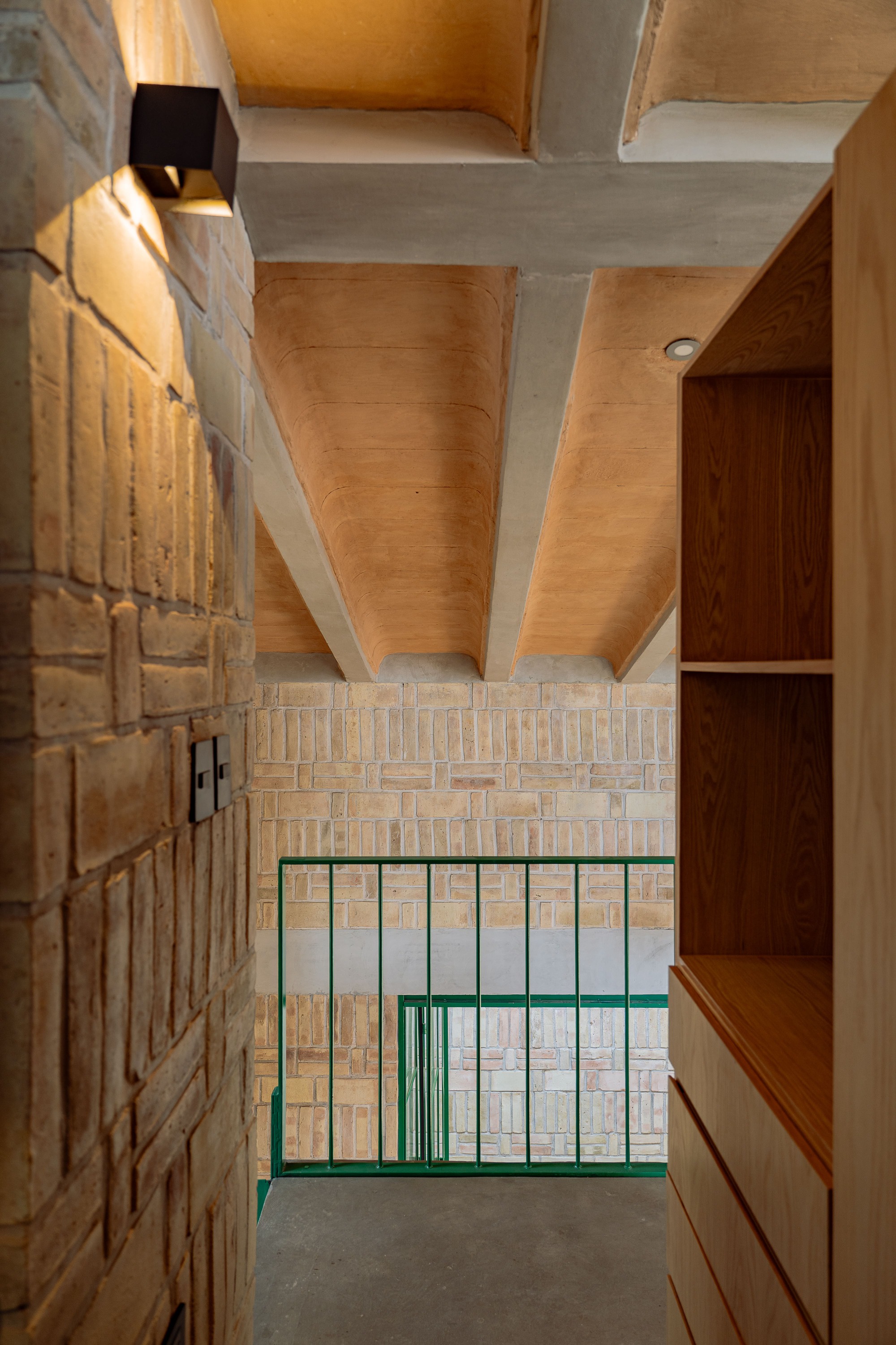 View down into entry hall showing concrete beams, timber ceiling and green steel balustrade