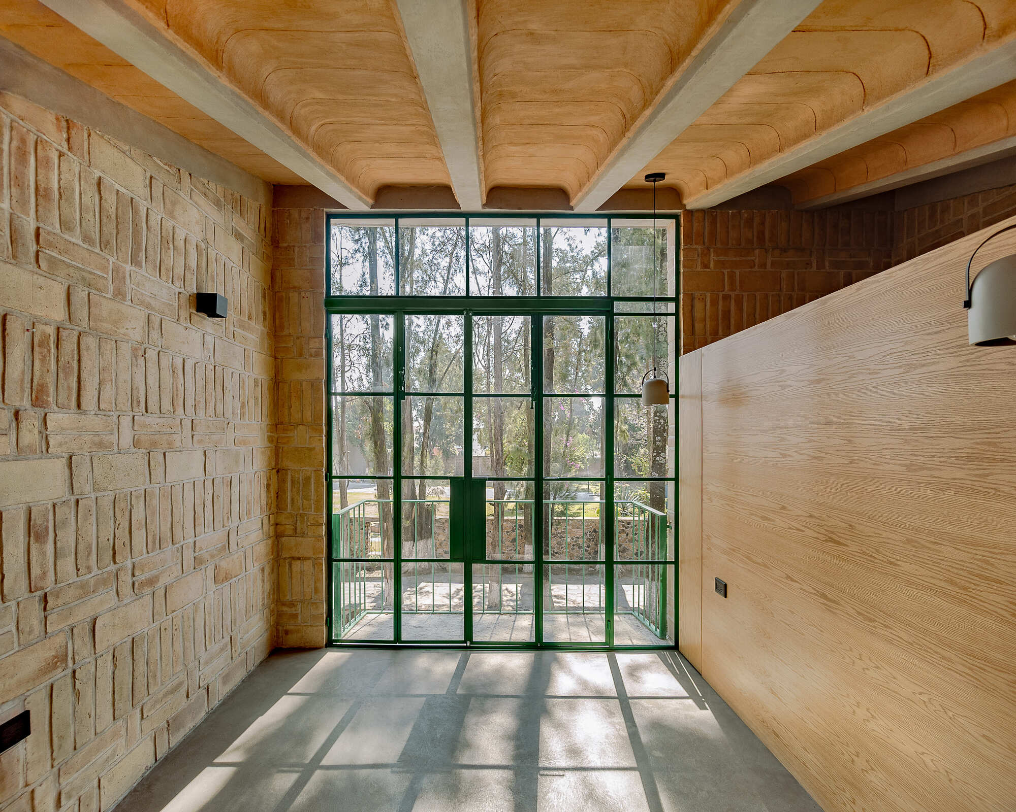 Full-height green steel window wall casting gridded shadows across polished concrete floor