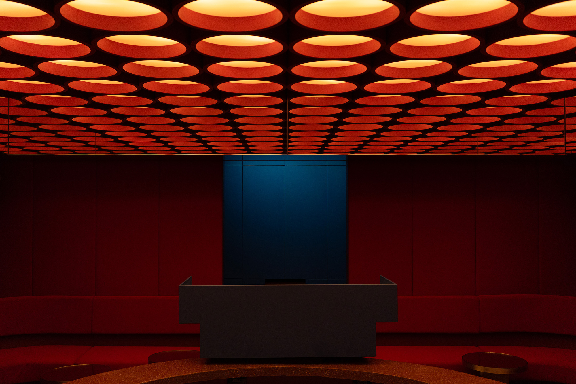 Interior view of the grid of circular orange ceiling lights above a black display counter in a red room