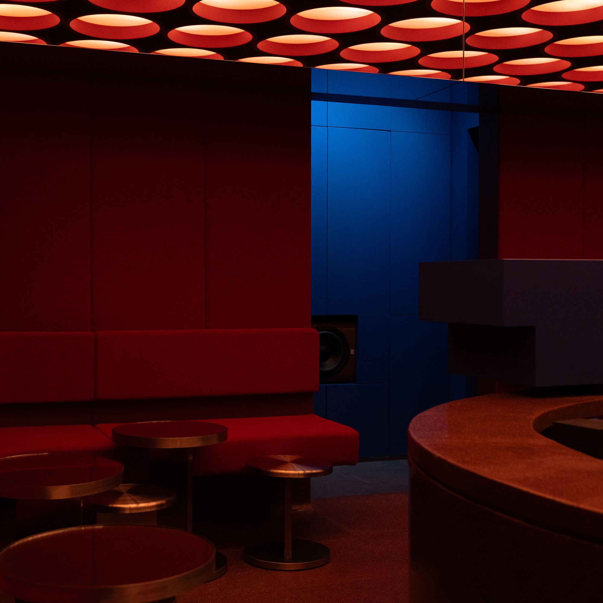 Blue paneled column against red walls with circular ceiling lights and bronze ottomans in the foreground
