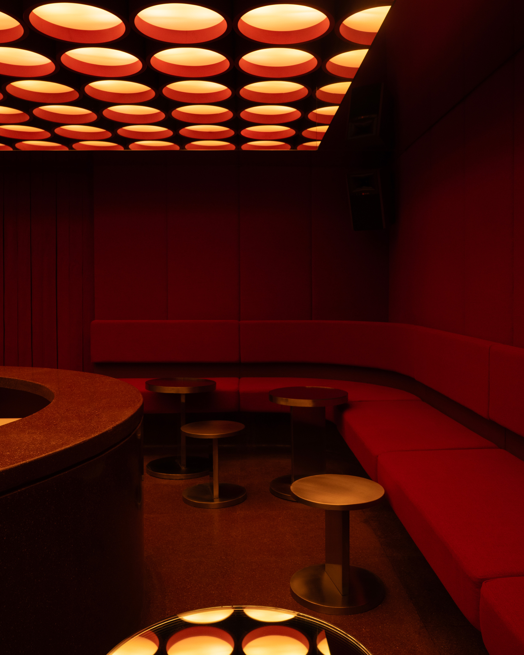 Corner banquette seating with bronze pedestal stools beneath the array of orange circular ceiling lights