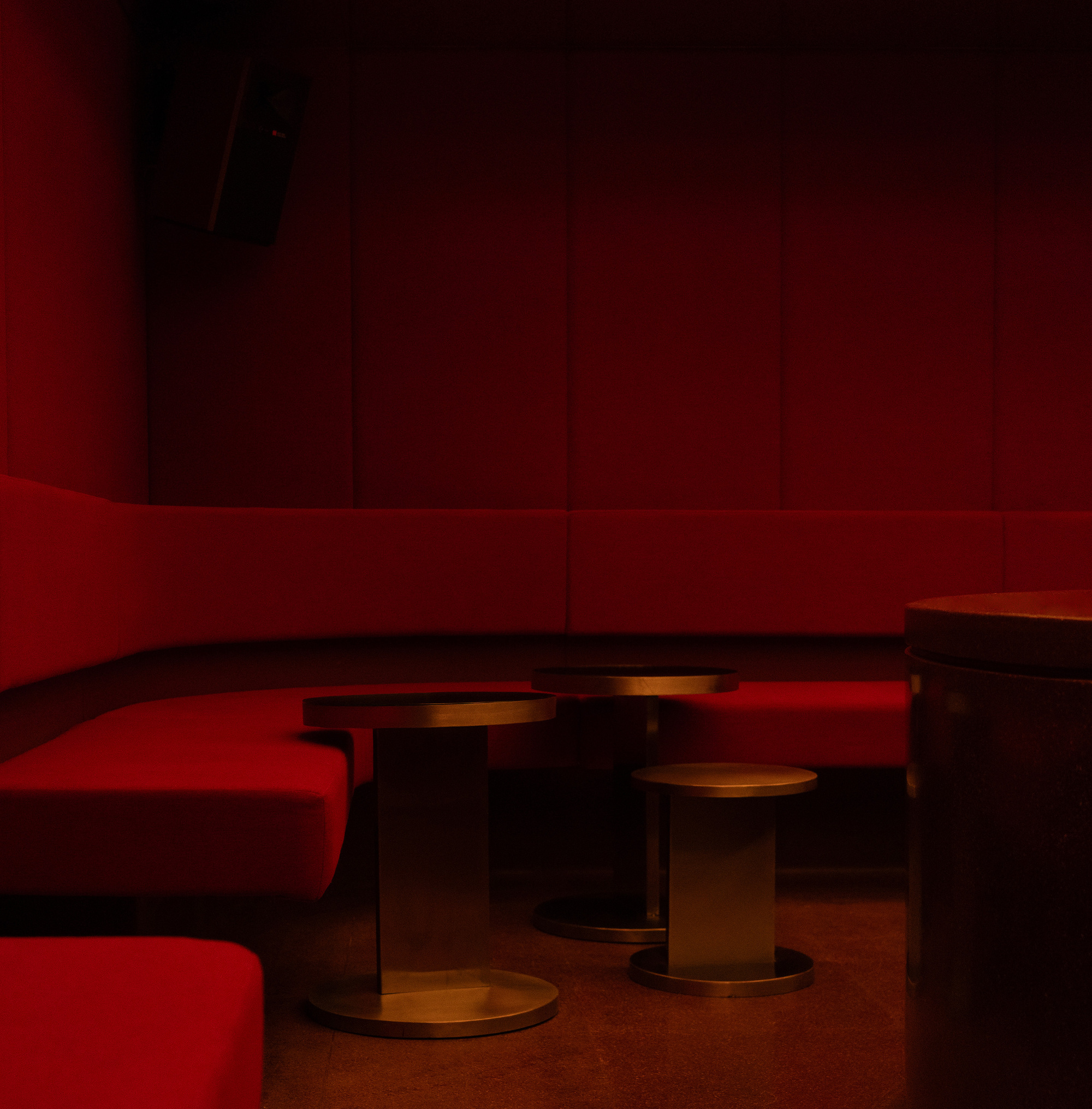 Interior lounge with red upholstered banquettes and bronze spool tables under dim ambient lighting