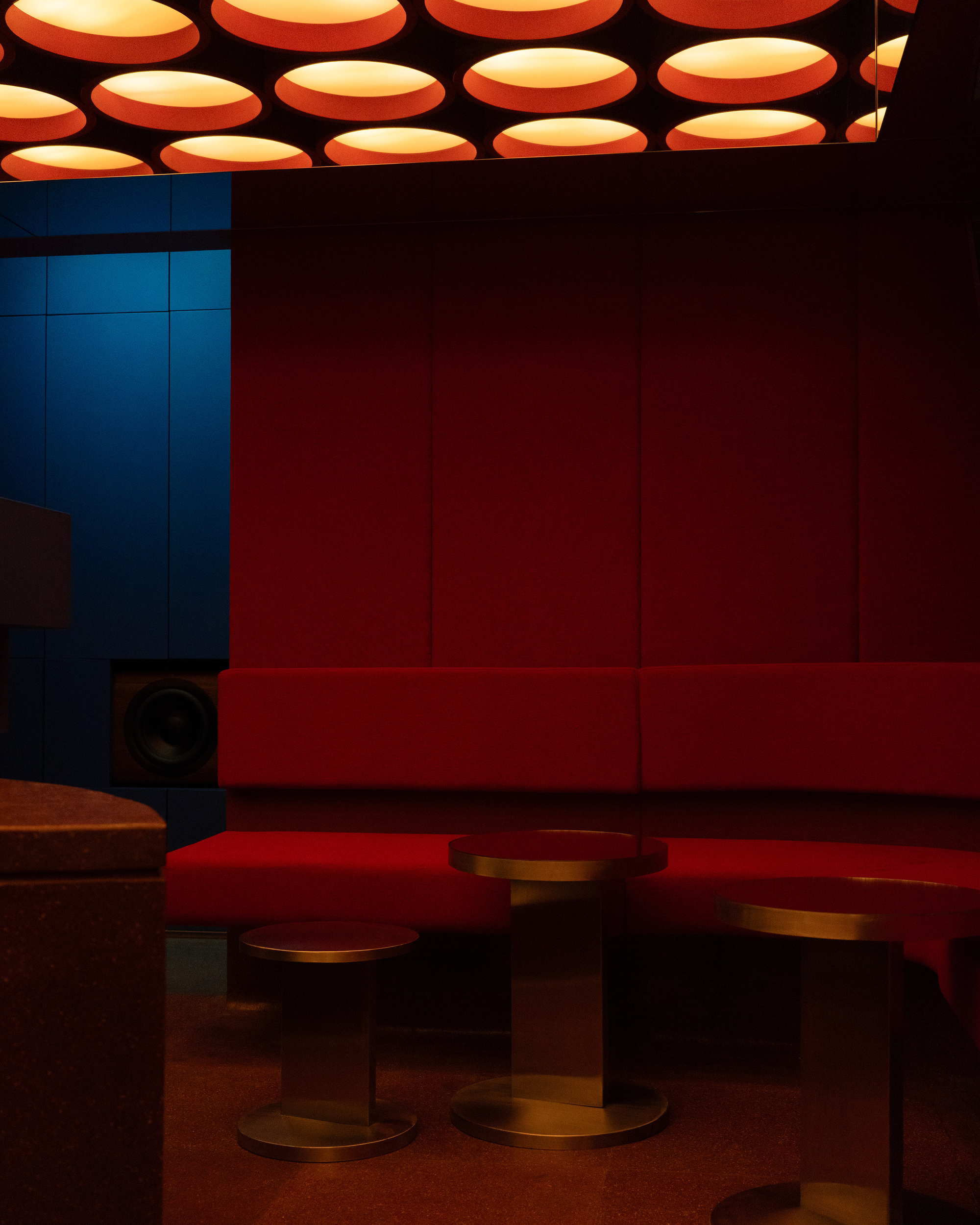 Red banquette seating beneath a ceiling grid of circular orange pendant lights