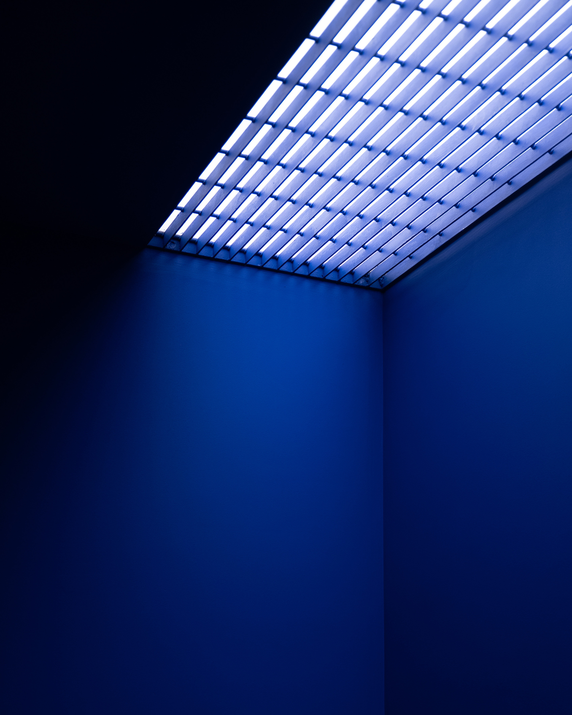 Corner view of a blue-lit room with a slatted luminous ceiling panel