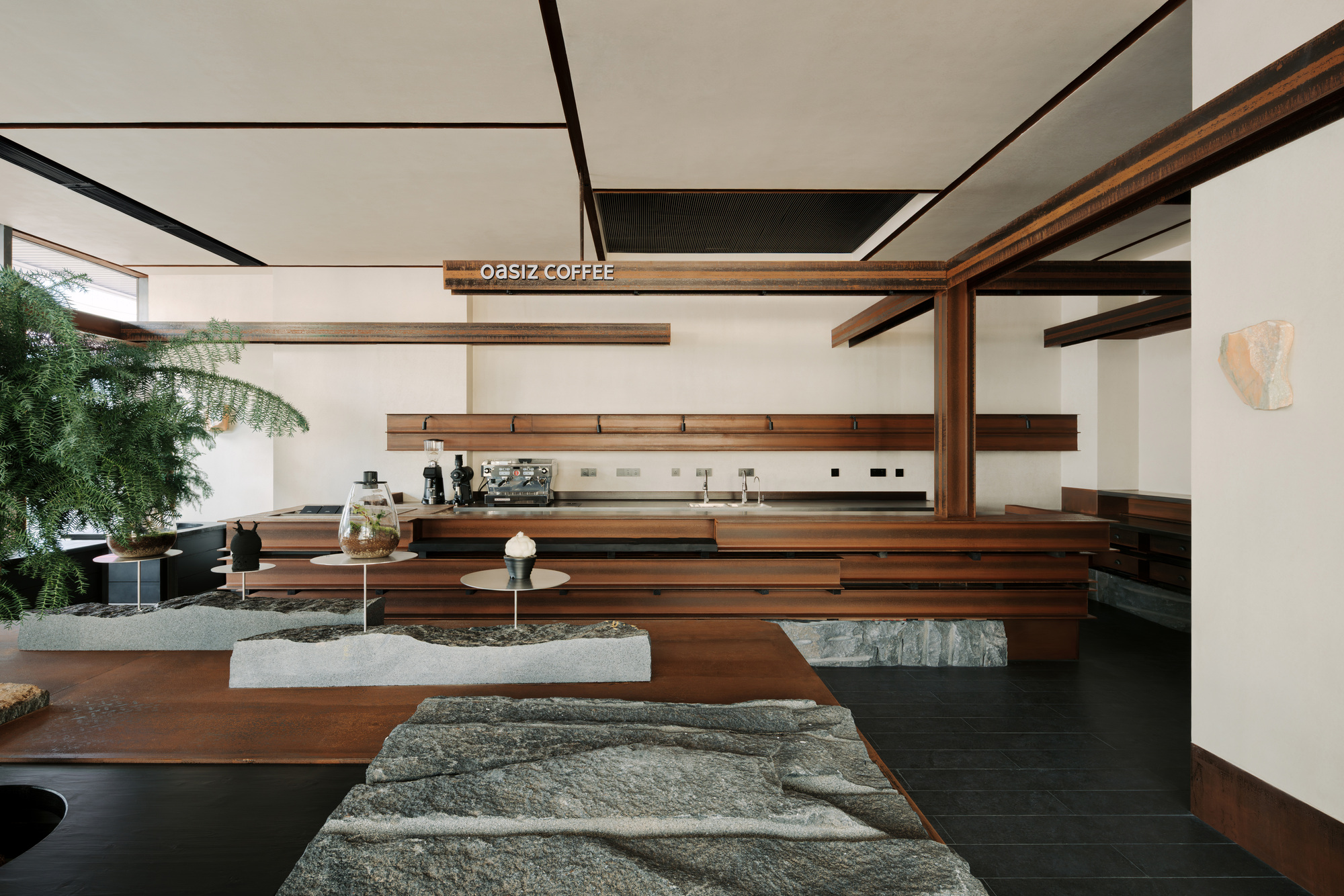Interior view of coffee bar with exposed timber beams, stone-topped seating platforms and potted palm tree