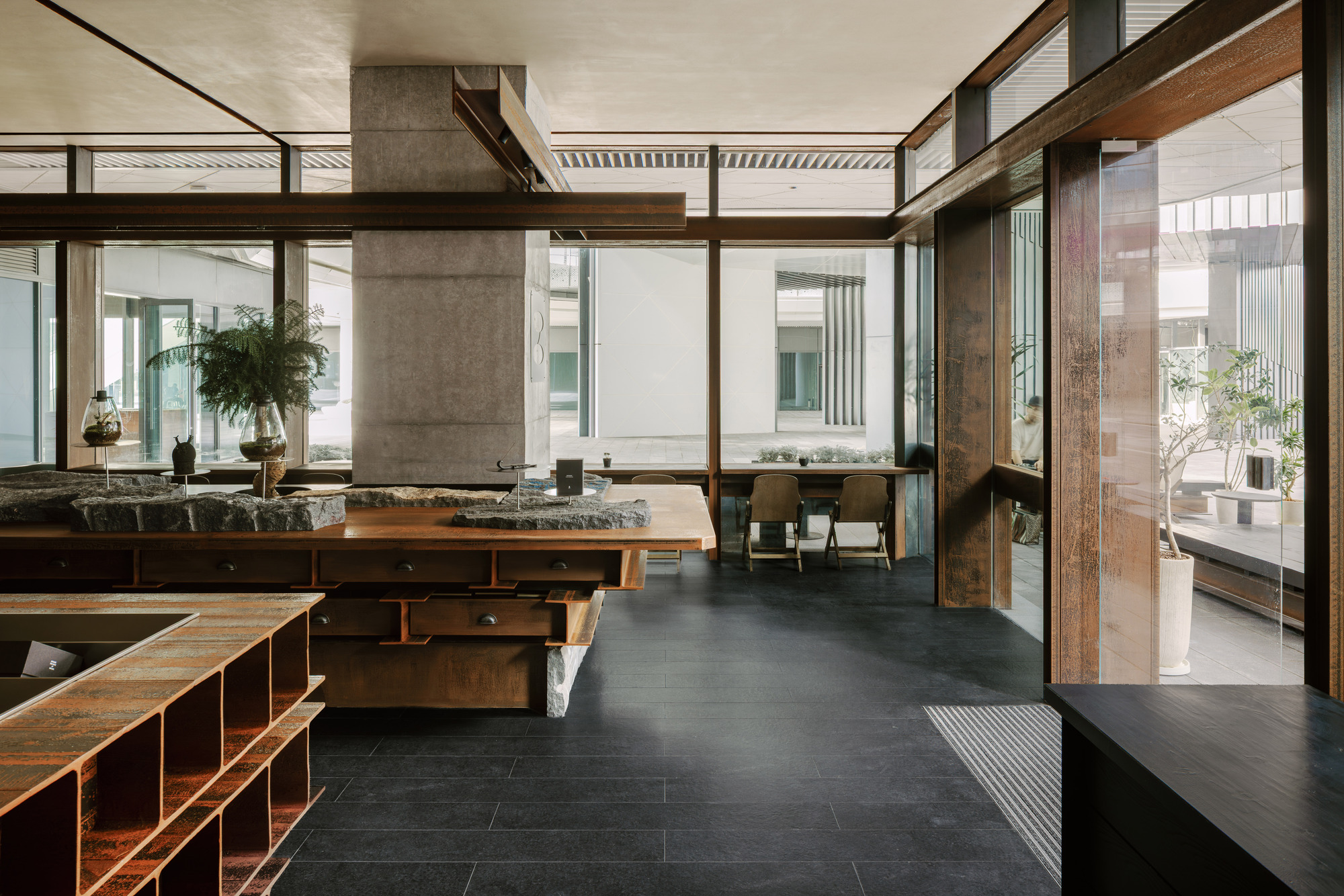 Interior looking through timber-framed glazing toward courtyard with concrete column and dining area beyond