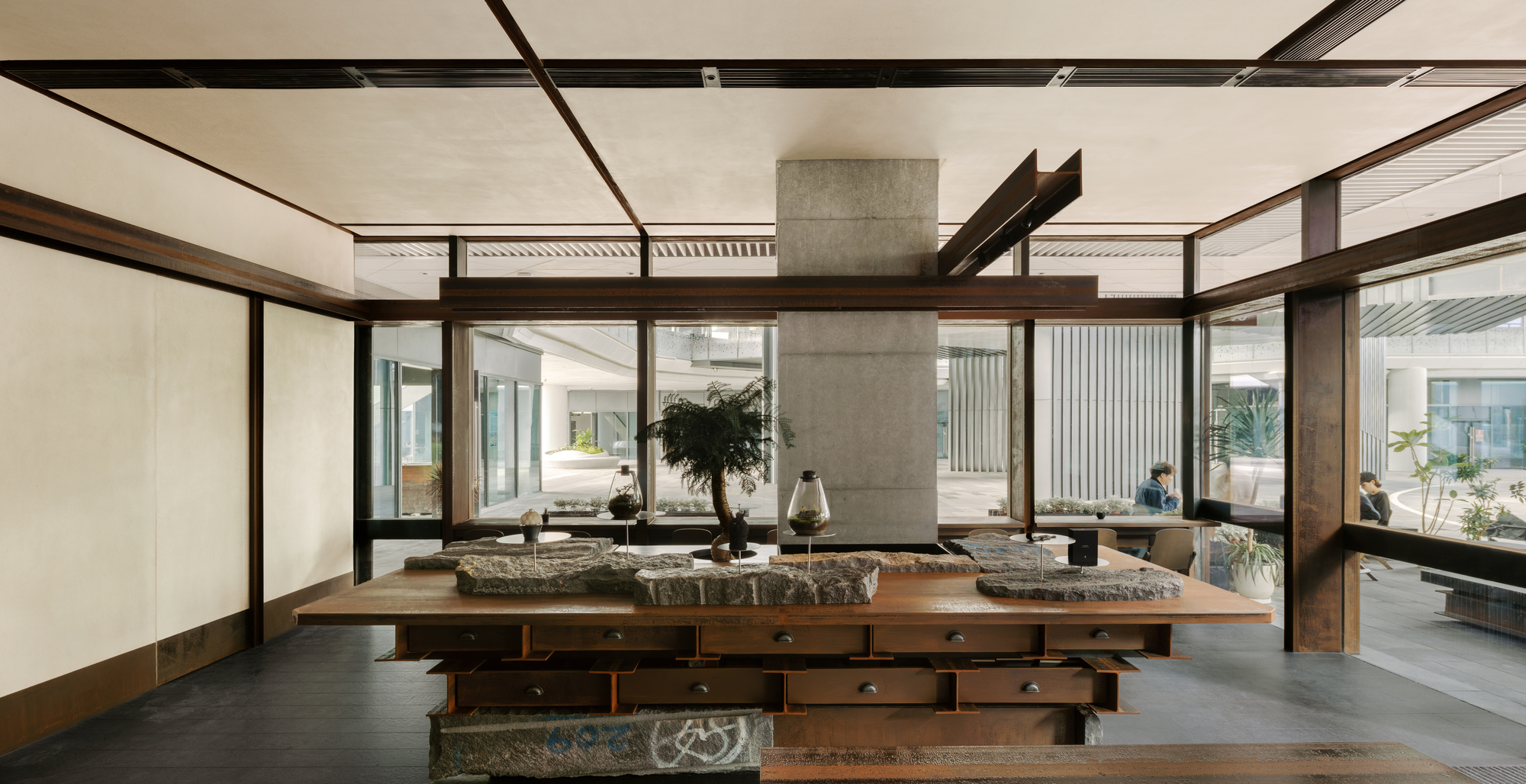 Wide view of the communal table with stone surfaces surrounded by glazed walls opening to courtyard