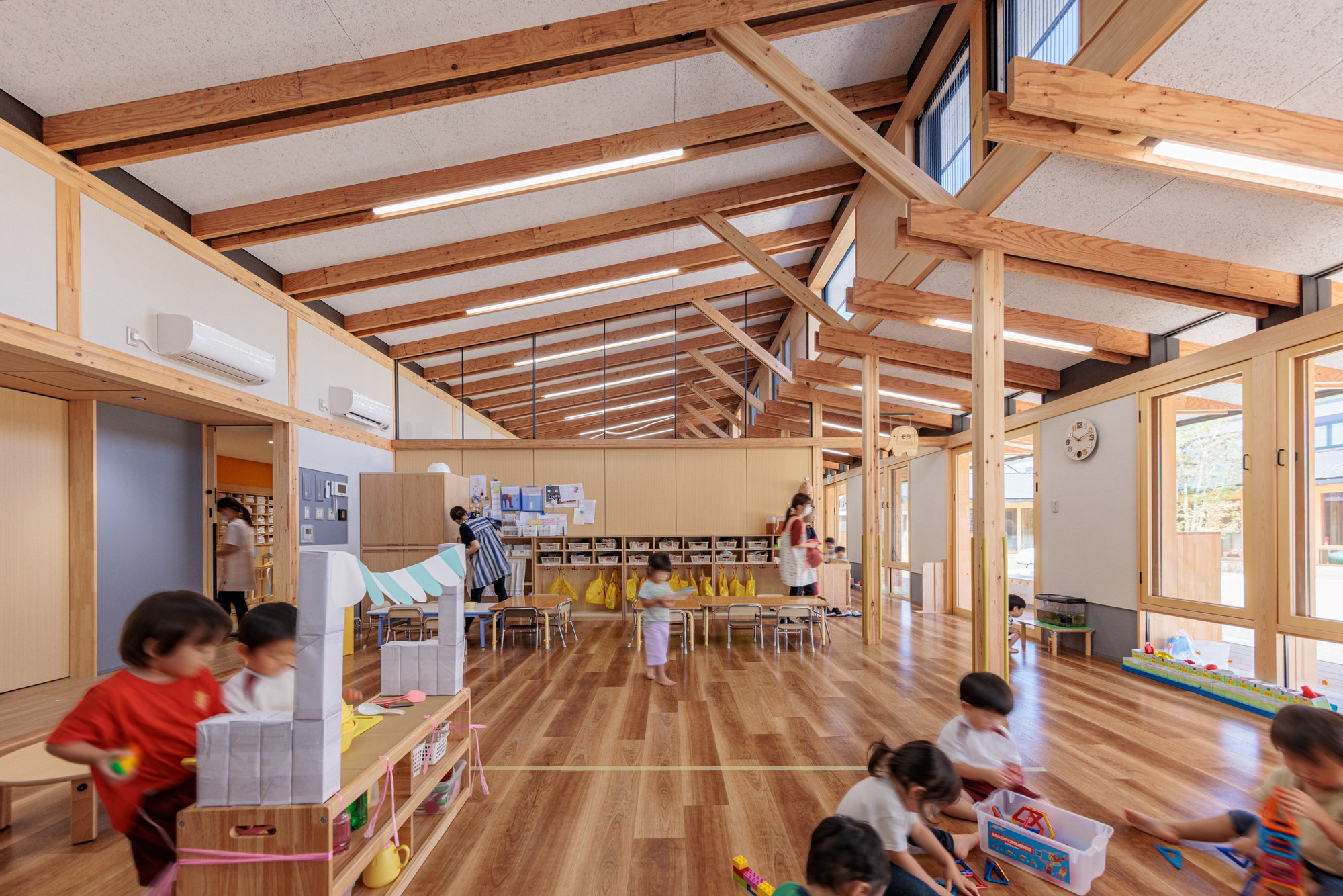 Interior view of the exposed timber roof structure with skylights above children playing on the wood floor