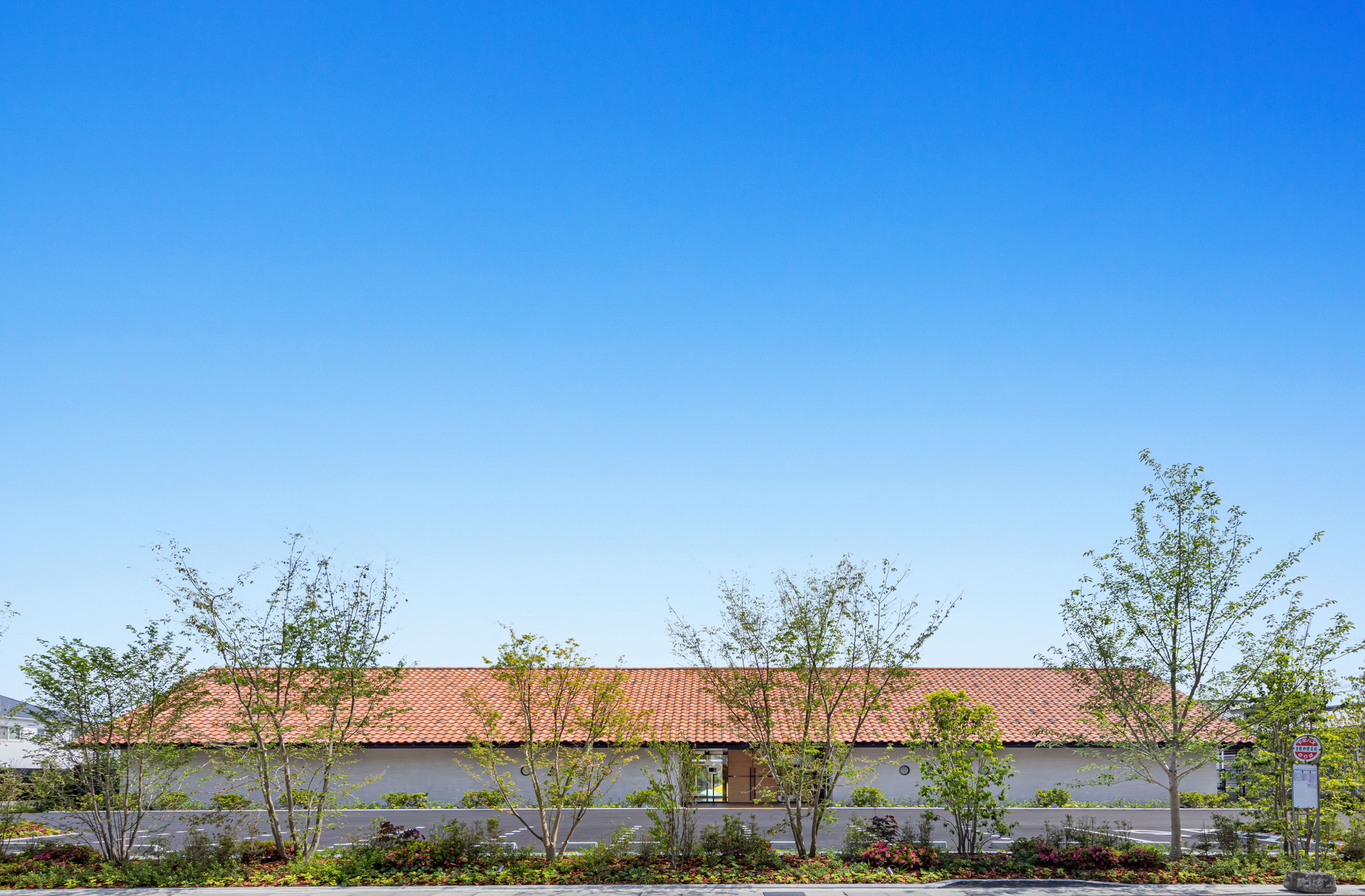 Long elevation showing the red tile roof with white stucco walls and young trees planted along the perimeter