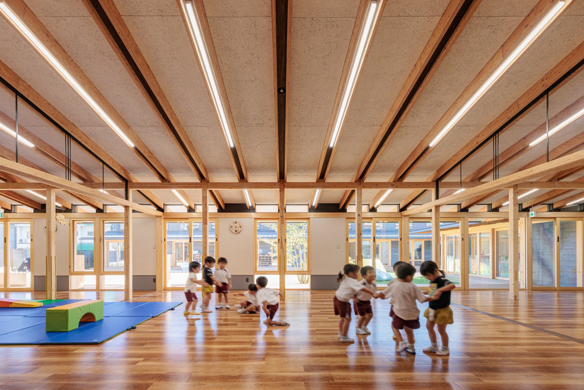 Open classroom space with timber beams and integrated linear lighting as children gather on the floor