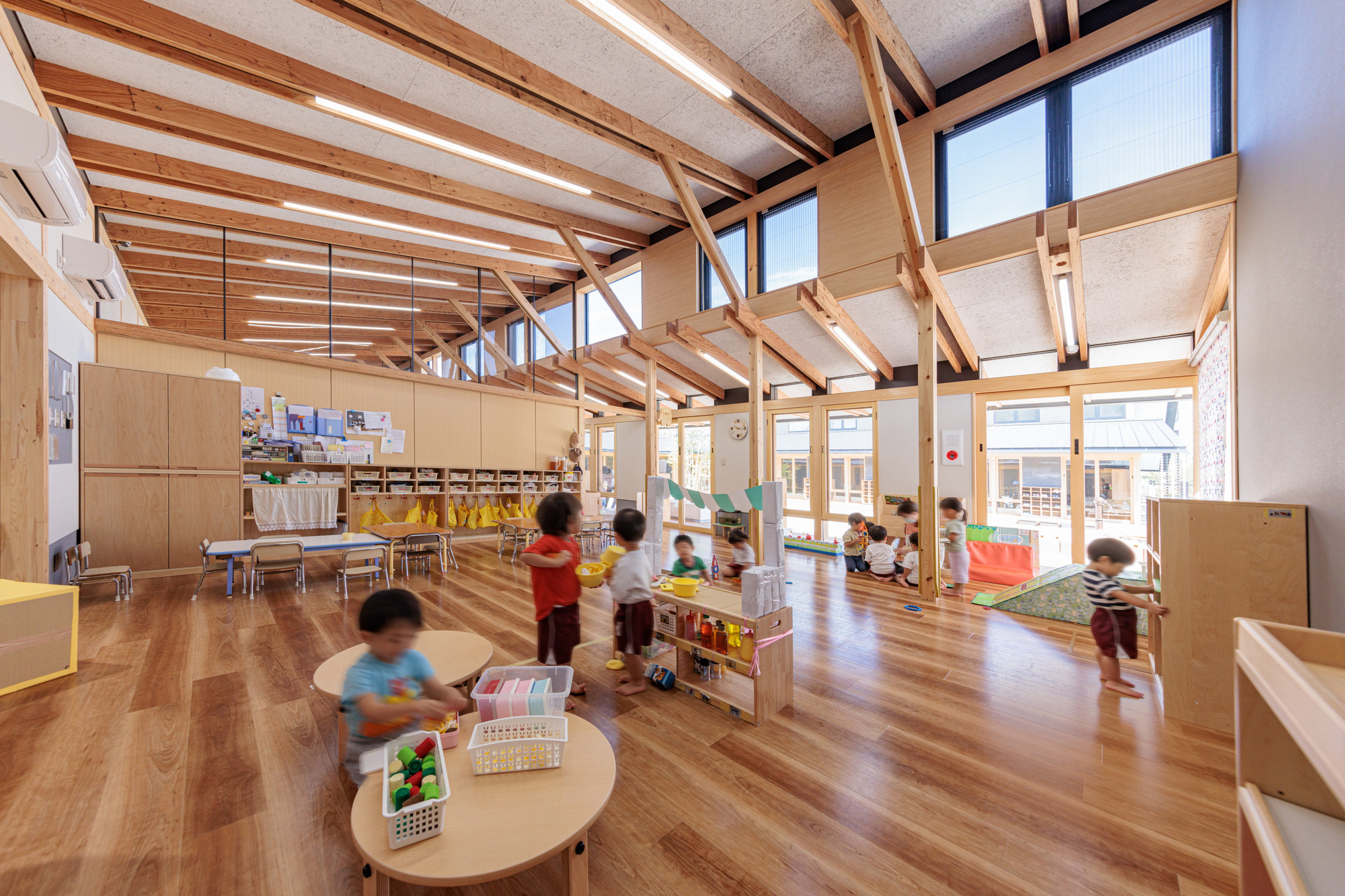 High ceiling volume with timber frame and clerestory windows above children moving through the play area