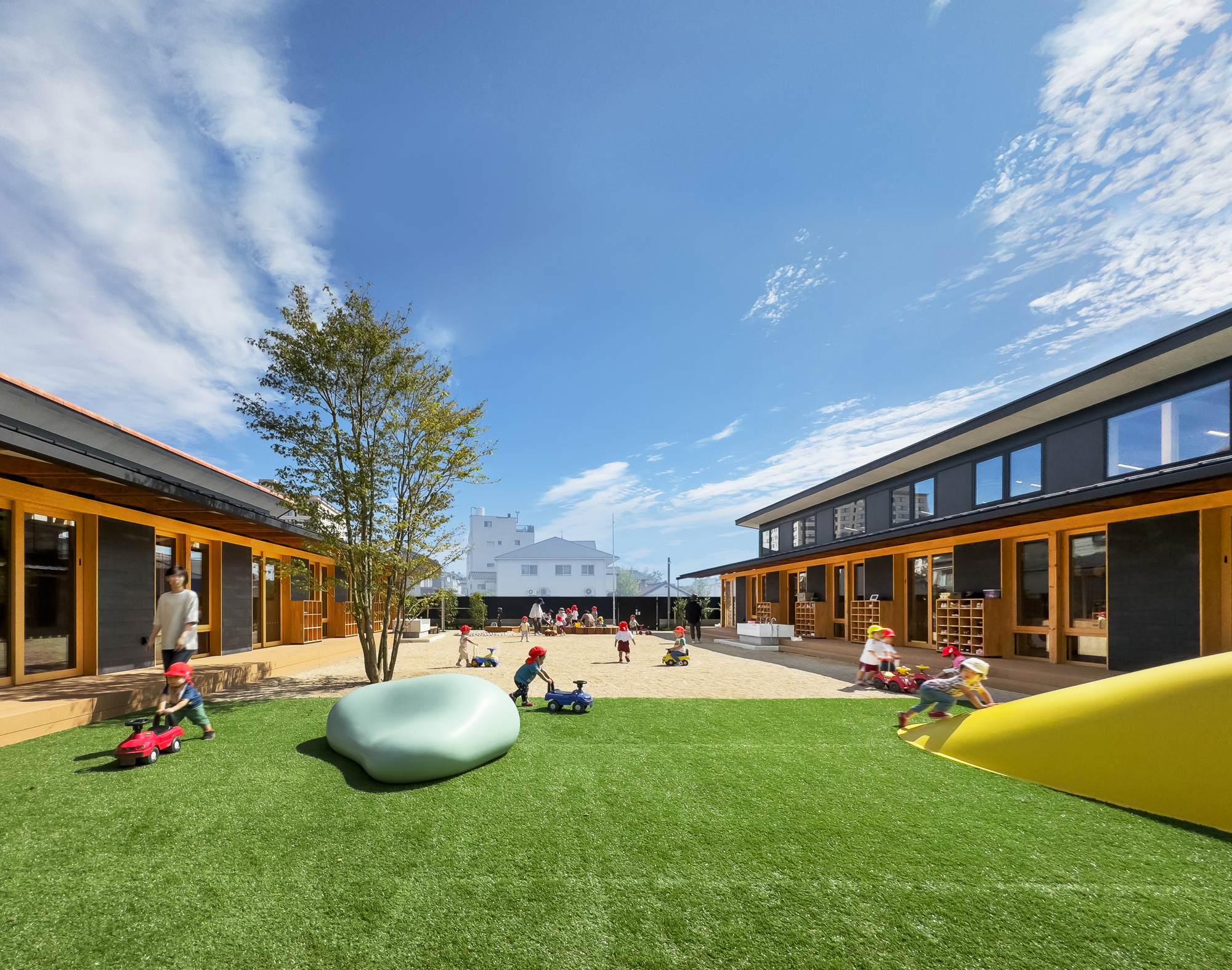 Central courtyard with synthetic turf and sculptural play elements between two low wings under a blue sky