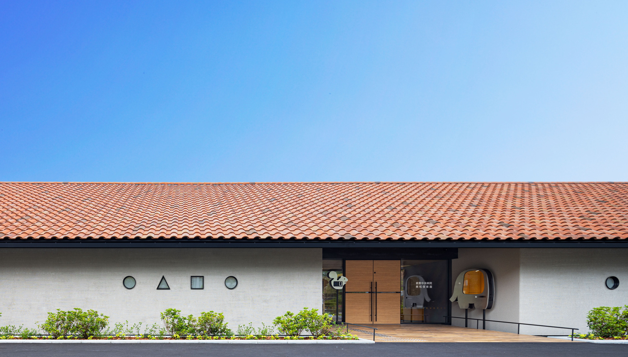 Entrance facade with geometric window openings in white stucco beneath the red tile roof