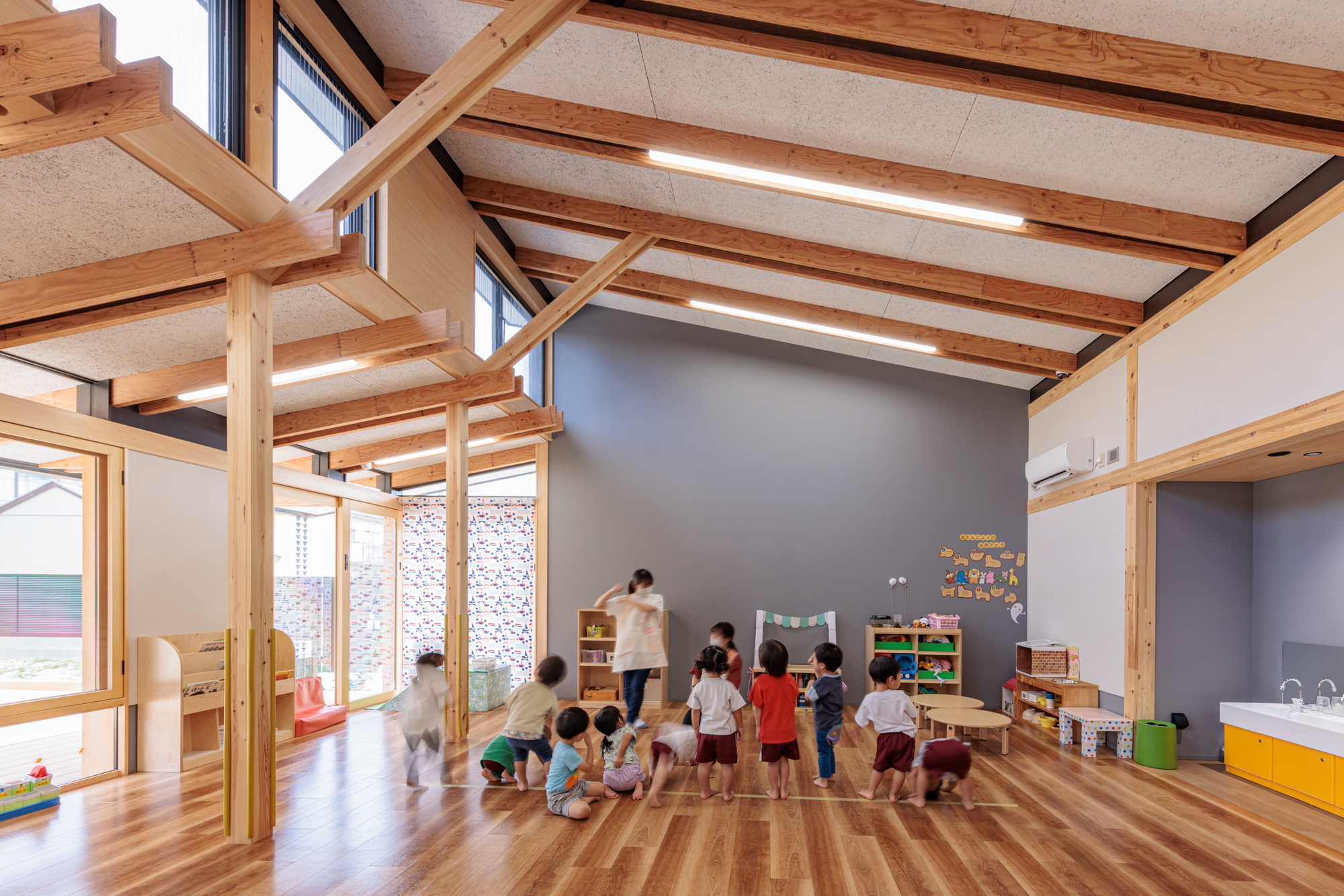 Classroom with exposed timber beams and ceiling panels where children gather on the wood floor