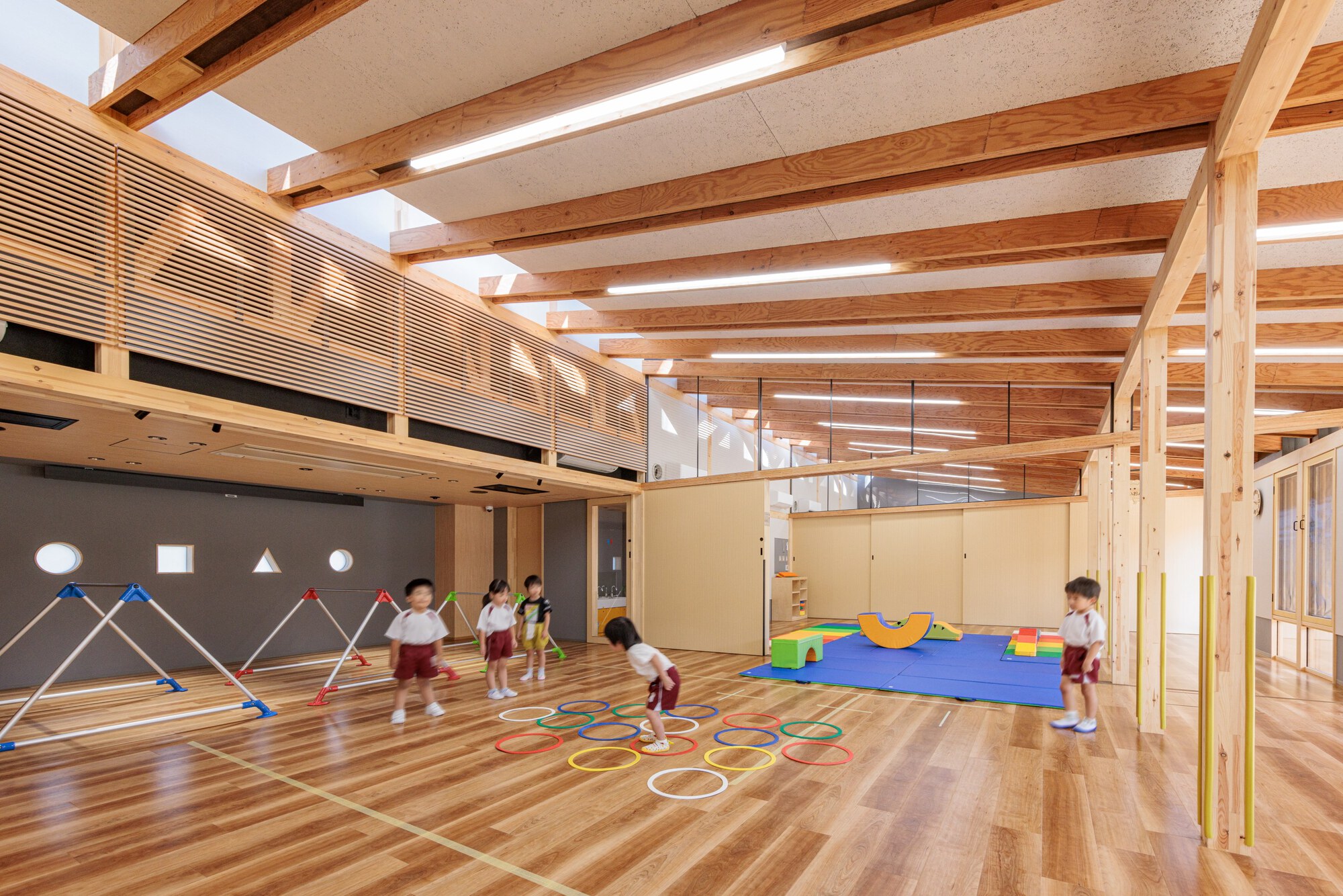 Play space with horizontal timber slat screen and mezzanine level where children use hoops and mats