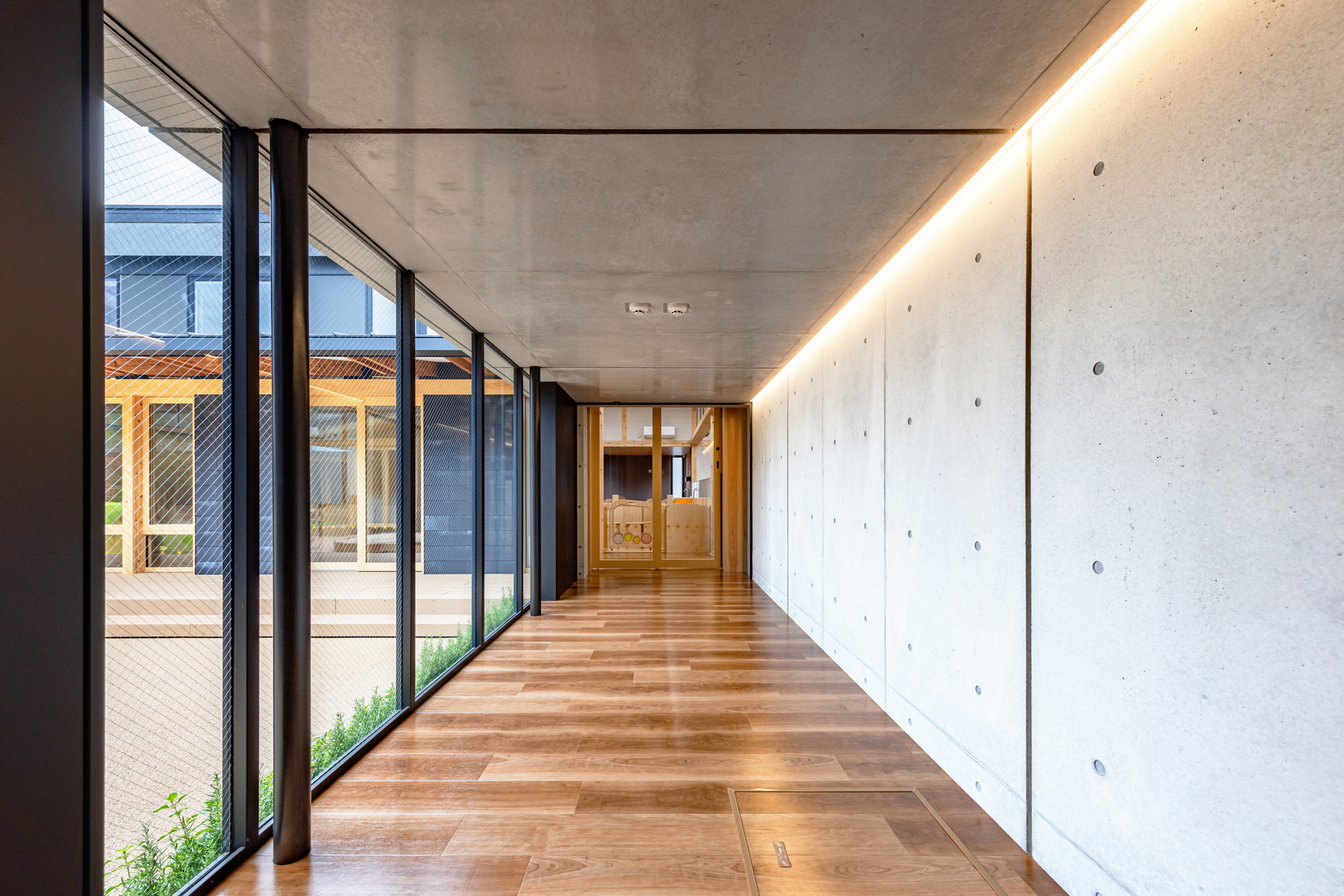 Corridor with poured concrete wall and recessed linear ceiling lighting alongside glazed courtyard doors