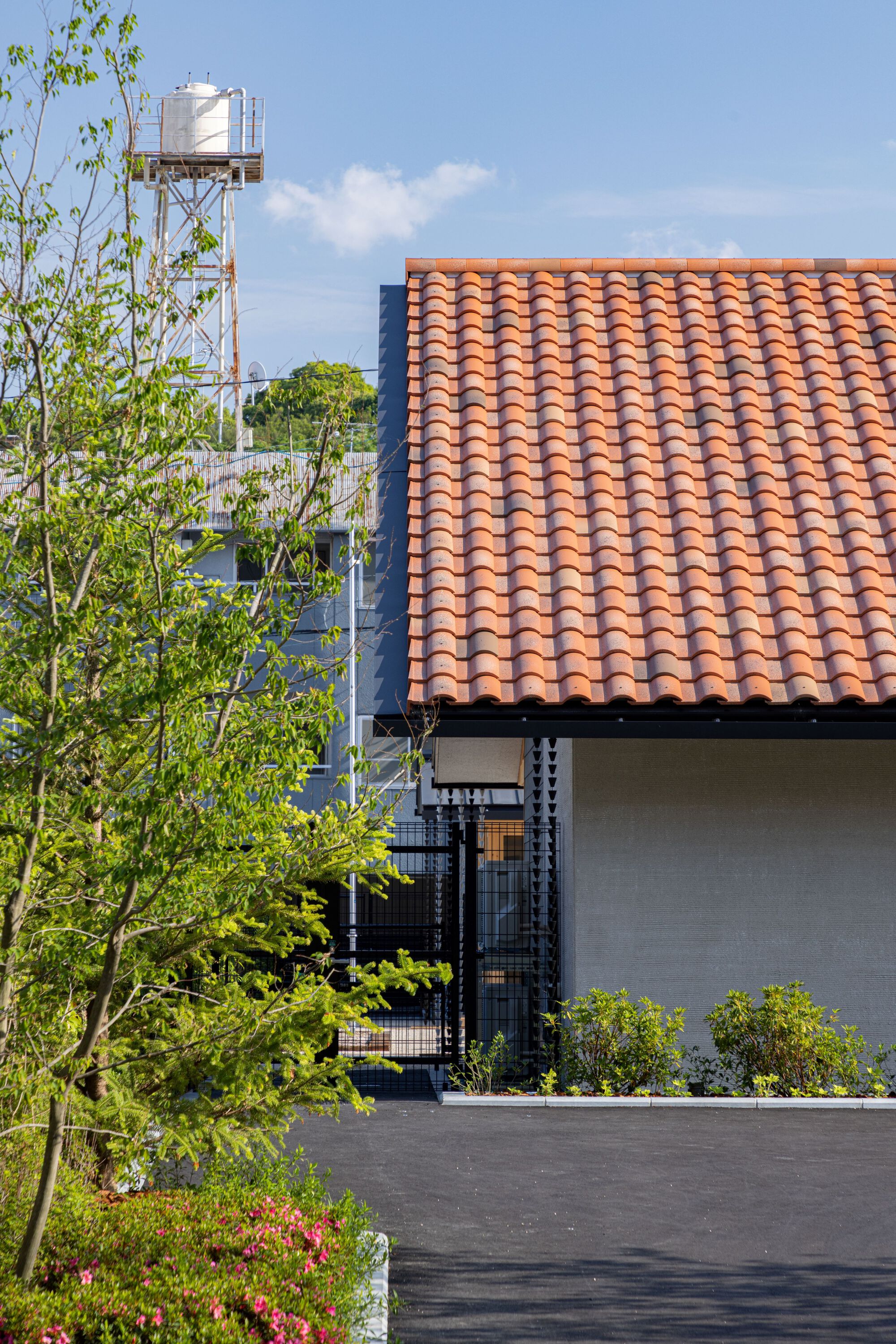 Orange clay tile roof with a planted bed of young trees and a water tower in the background