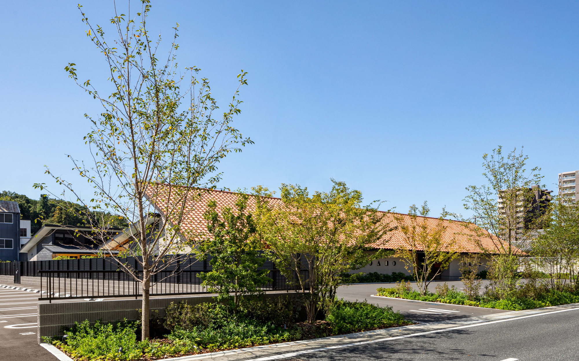 Street view of the clay tile roofline with young trees framing the planted perimeter