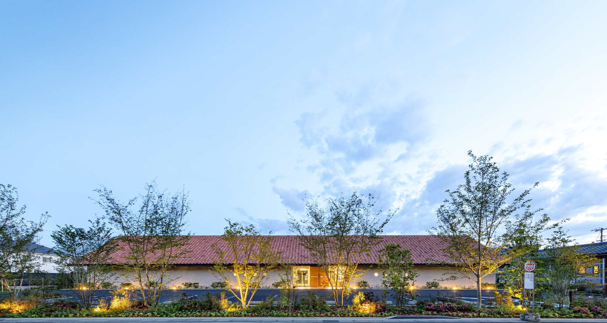 Long facade with uplighting highlighting young trees at dusk