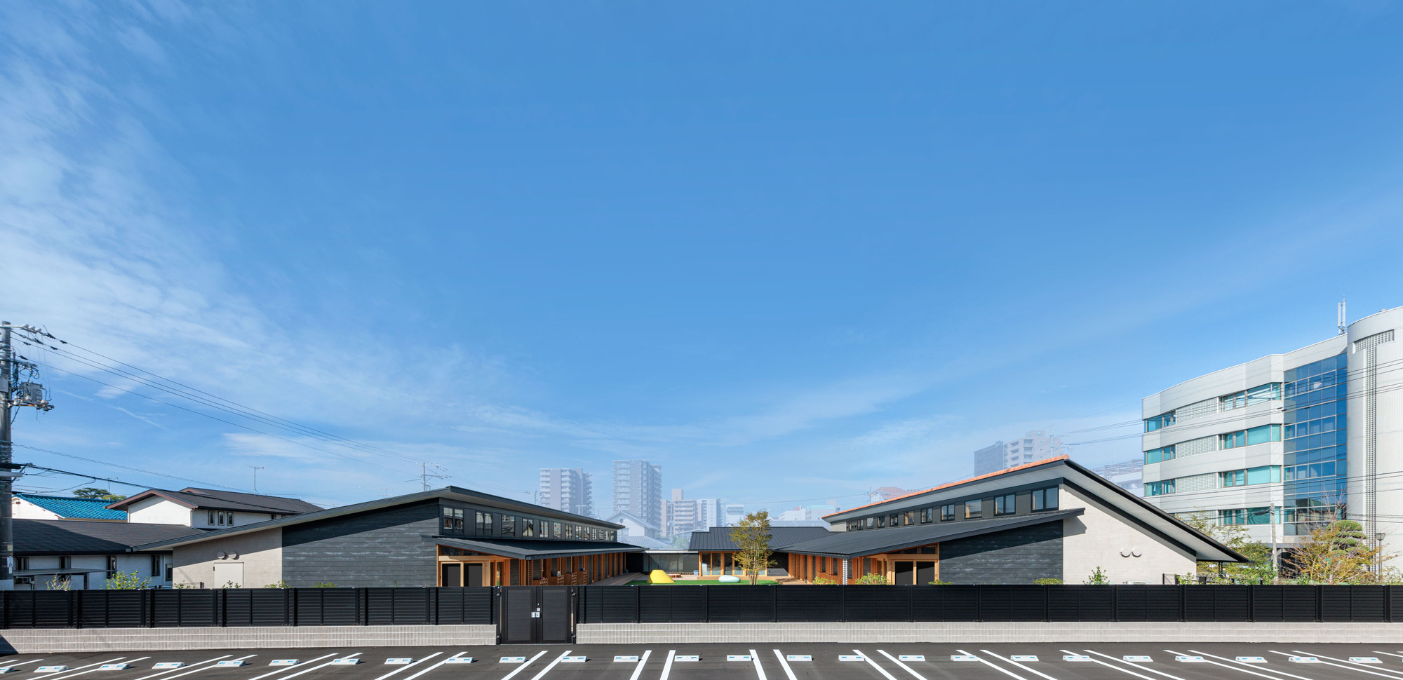 Street view showing two gabled volumes with dark cladding and a connecting central section